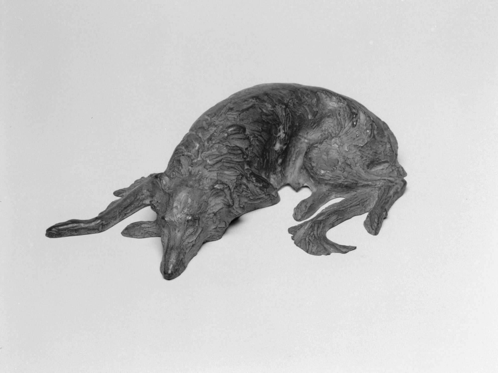 Statuette of a hound lying down with head resting on front paw; rear legs and tail under proper left side of body; highly textured surface.