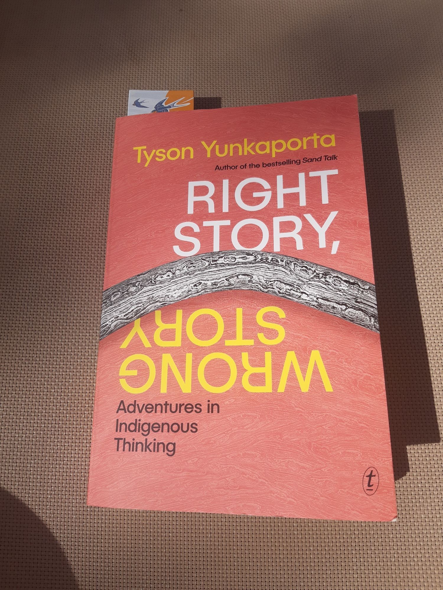 Front cover of Right Story Wrong Story: Adventures in Indigenous Thinking by Tyson Yunkaporta. Red cover with a grey boomerang across the middle.