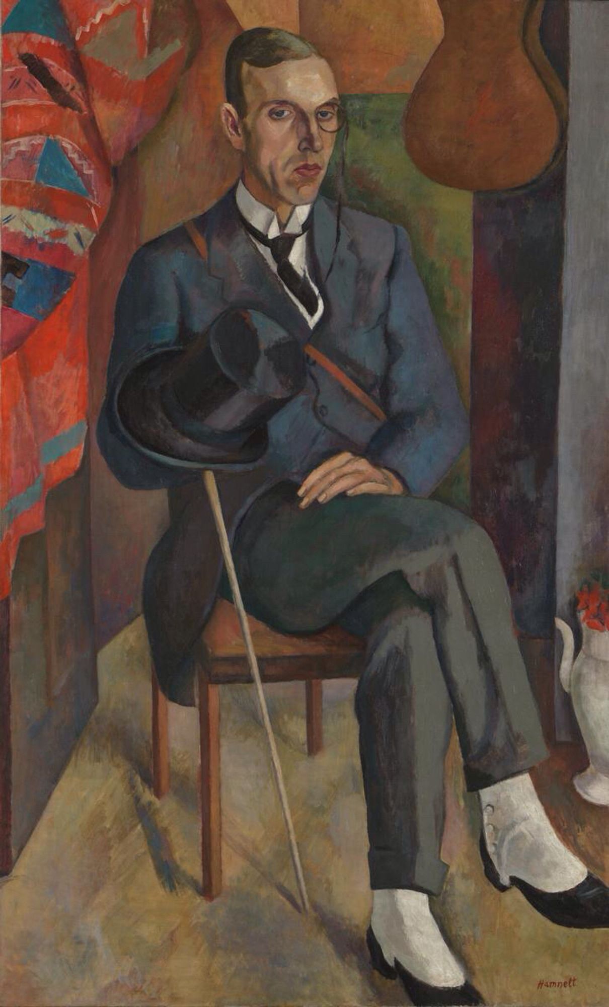 A slightly stylised portrait of a man sat on a wooden chair. He wears a gray formal suit whose jacket has tails. His right leg is crossed over his left. He wears black shoes with white spats. His left hand rests on his right thigh and his right hand is hidden inside a black top hat and holds the top of a thin cane that sticks out towards the floor. A brightly patterned cloth hangs on the left of the picture and a guitar hangs on the wall on the right.