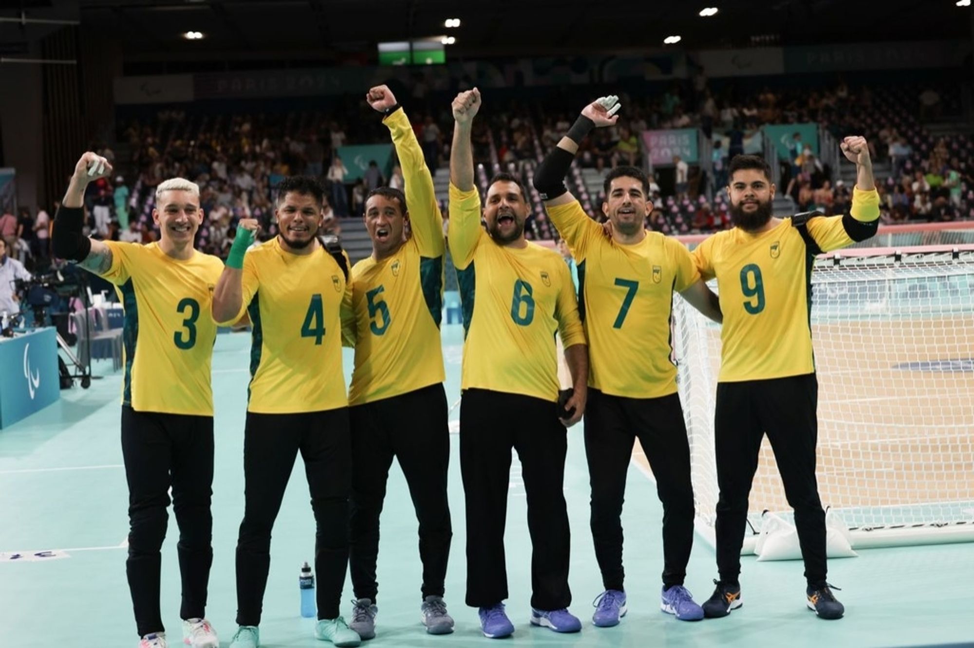 Paulinho, Leomon, Parazinho, Romário, Emerson e Dantas estão bem de frente para a câmera e vibram após a vitória sobre o Egito. Eles vestem camisa amarela de manga longa com os números em verde na altura do peito e calças pretas. Dantas está perto de uma das traves da quadra na Arena Paris 6. Fotos; Alexandre Schneider/CPB