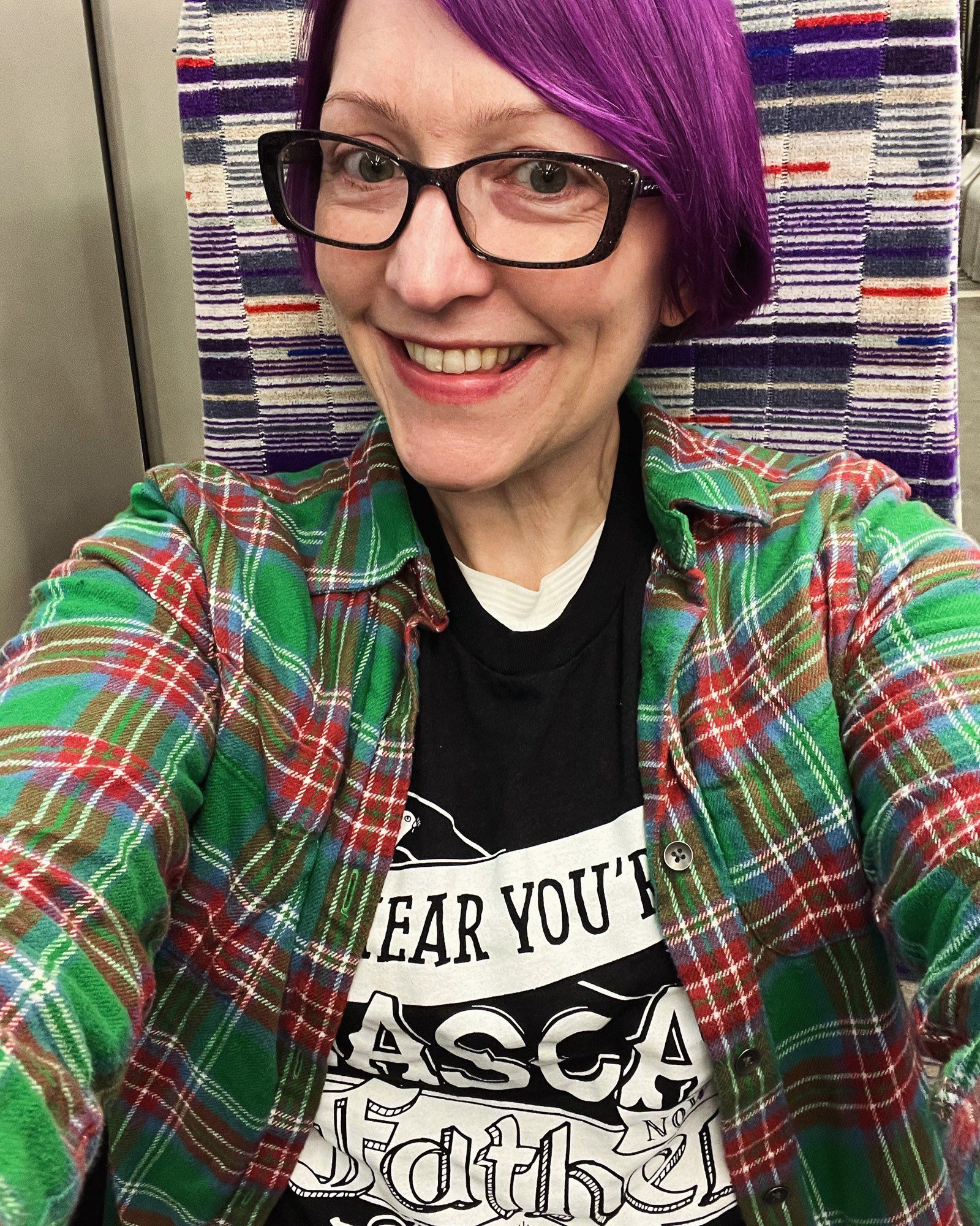 Pale white lady on the Elizabeth Line in a black Rascals Brewing t-shirt and green flannel top shirt