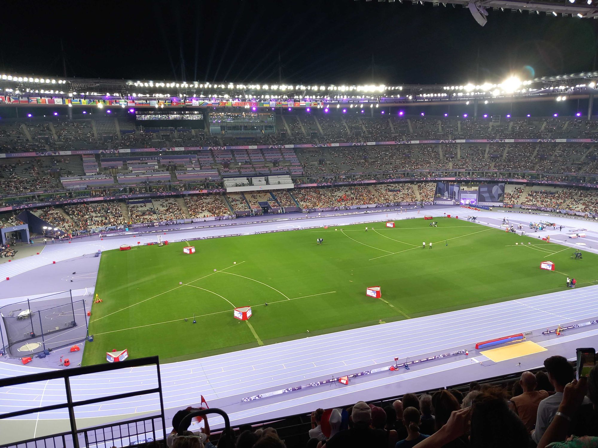 Photo d'ensemble de la pelouse, la poste et la tribune en face au Stade de France éclairé, de nuit.