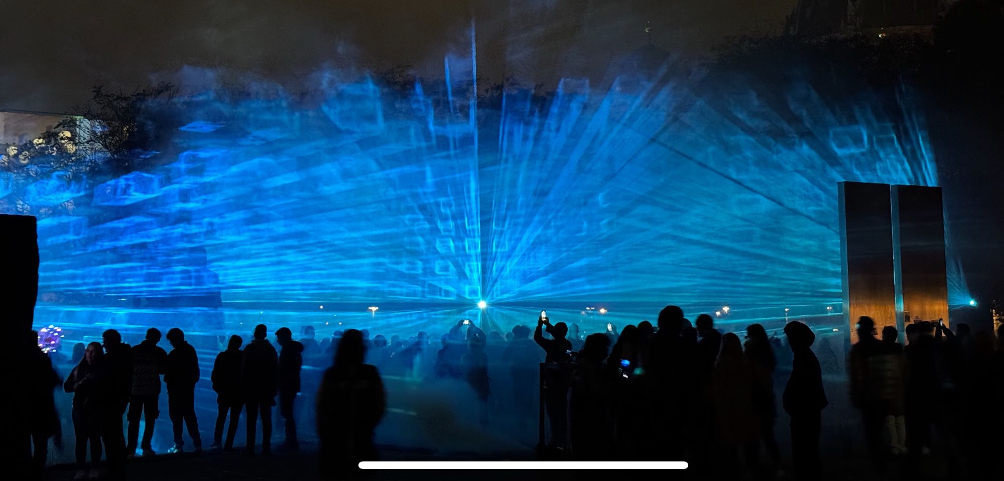 Lasershow mit geometrischen blauen Formen in Trockennebel, im Vordergrund Silhouetten von Menschen