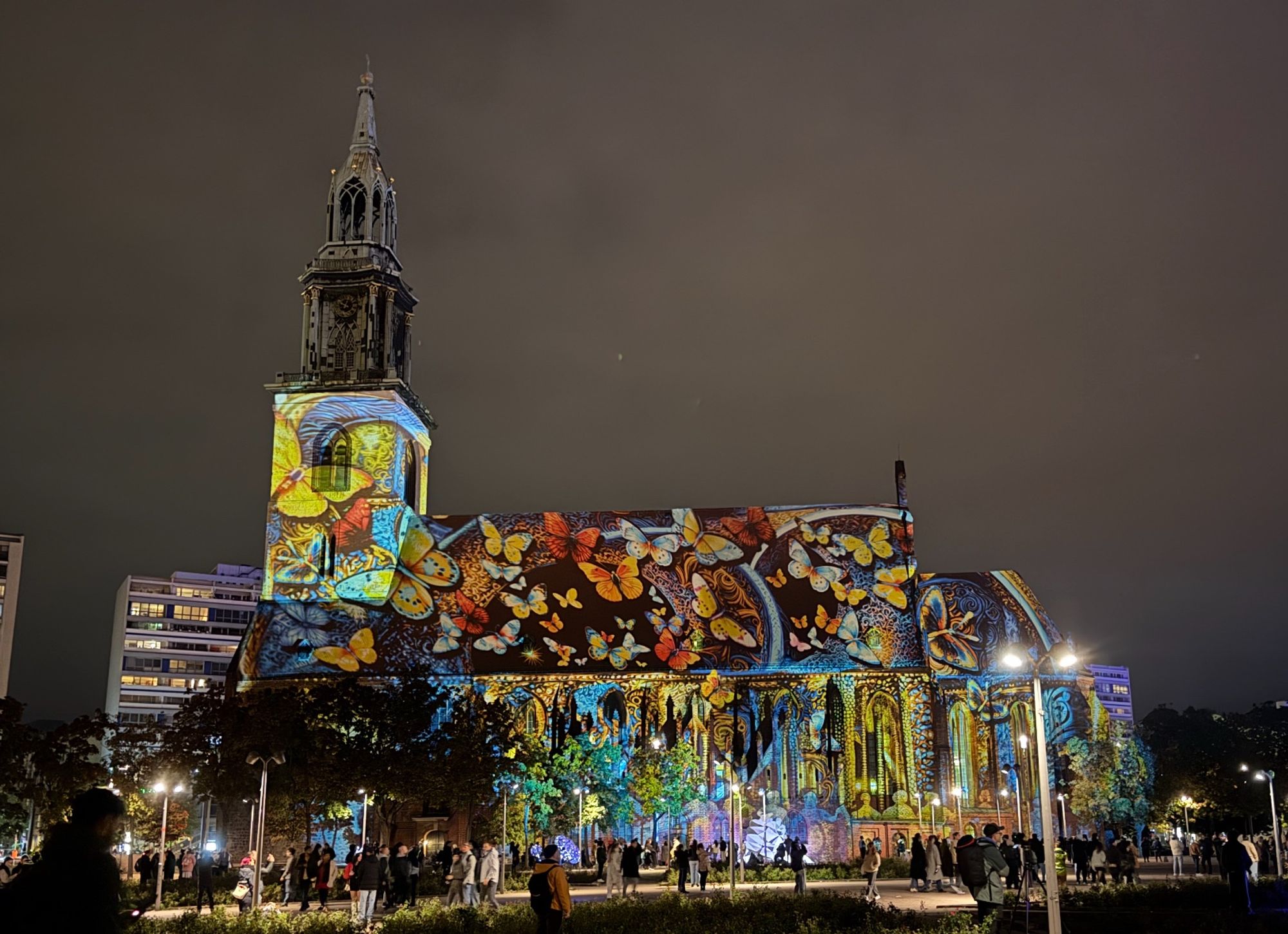 Marienkirche in Berlin von Süden vor nächtlichen bewölktem Himmel. Auf das Gebäude sind riesige bunte Schmetterlinge projiziert.