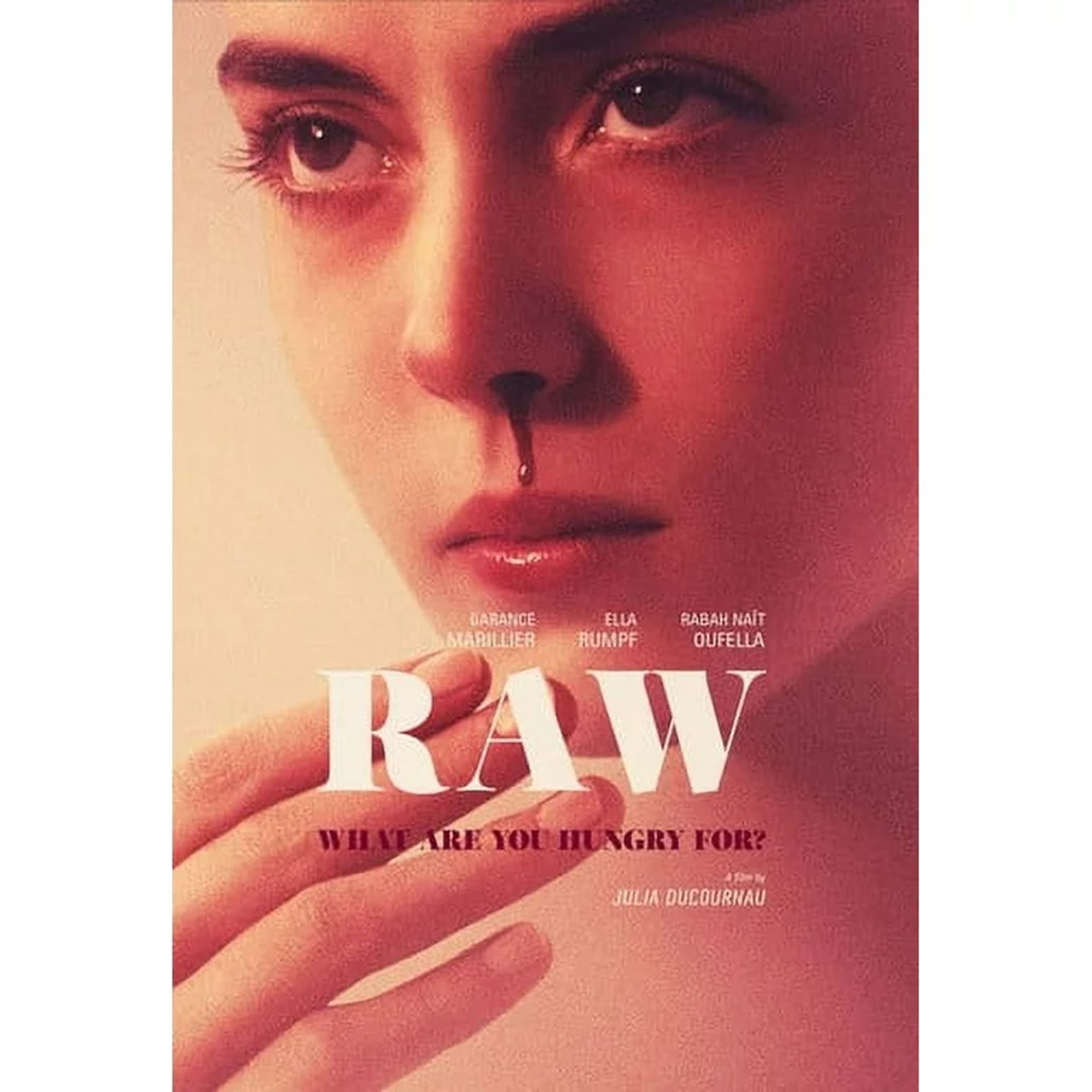 The same young white woman as the first image is bleeding from her left nostril, holding her hand in front of her face. She looks up through her lashes. The title of the film is 'RAW' in white serif font, with 'WHAT ARE YOU HUNGRY FOR?' beneath it.