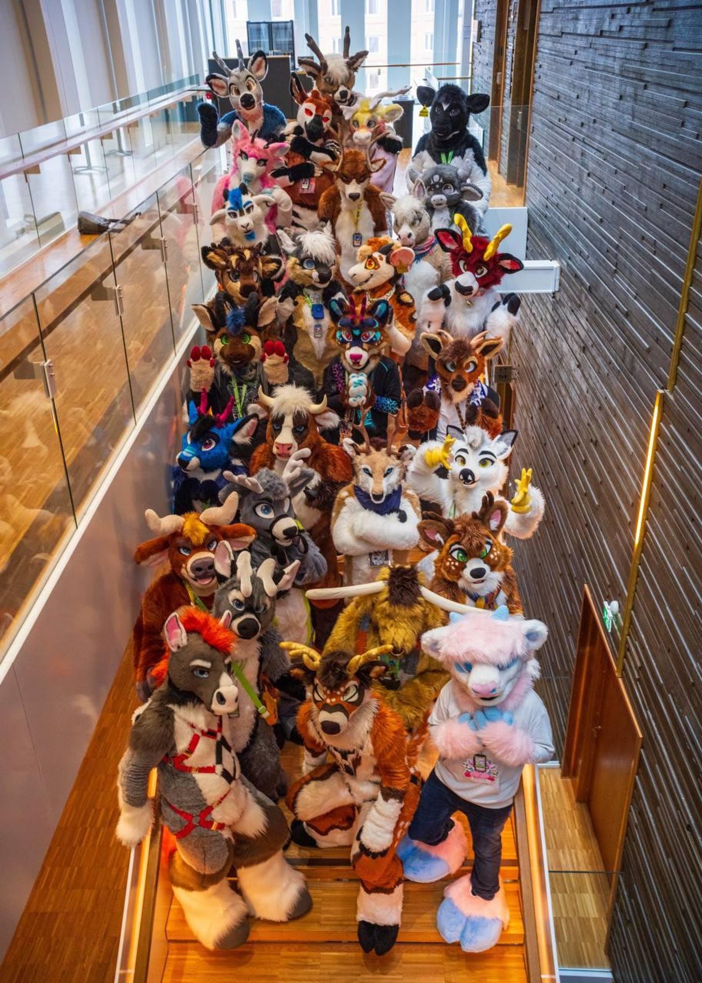 29 hooved fursuiters standing in a staircase, posing for the camera.