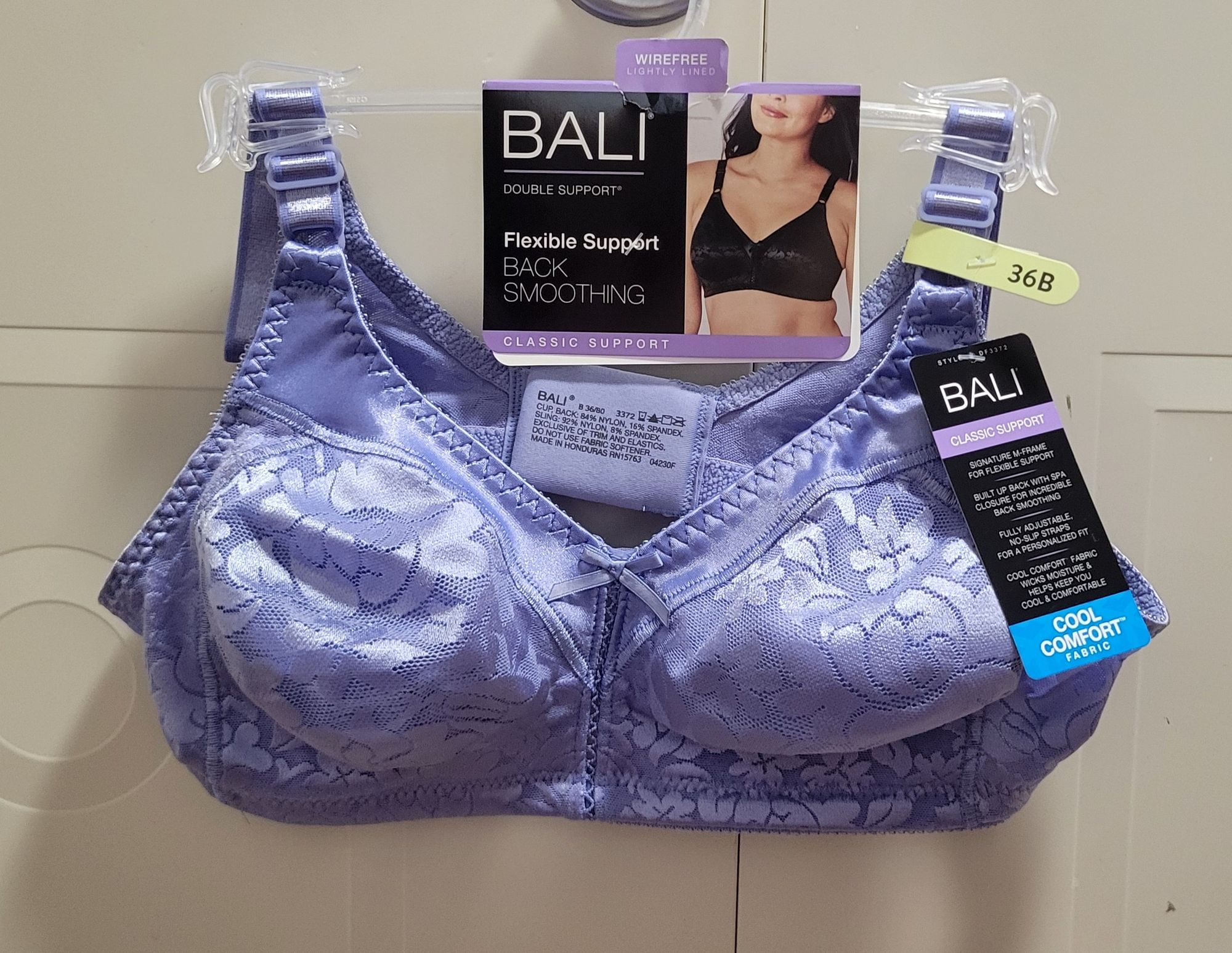 A brand new, light blue bra by Bali still on its hook, with tags hanging from the handle of a closet door.