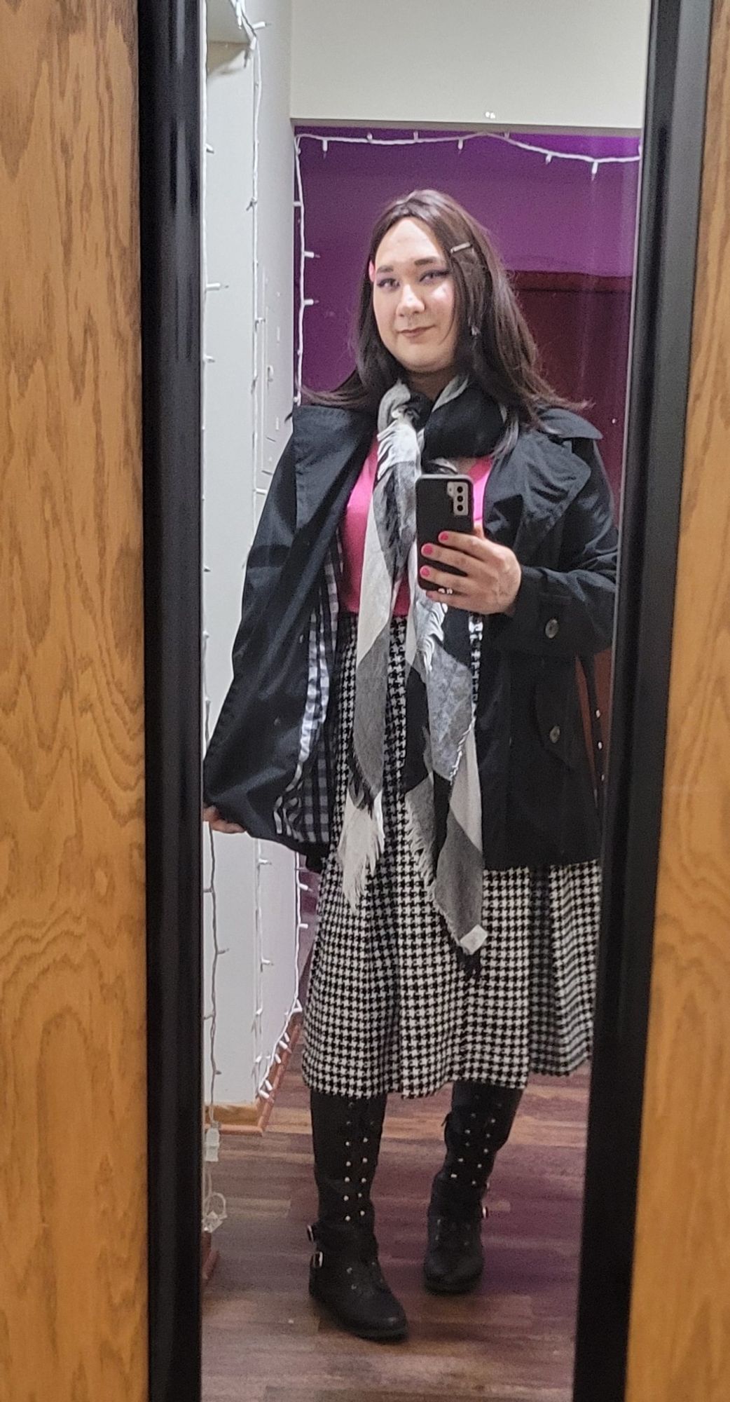 Suzies outfit: brunette hair, a black trench coat, long black and white plaid scarf, pleated houndstooth A-line skirt, pink tee shirt, tall black boots. She's holding her phone out, showing off her nails, painting fuchsia.