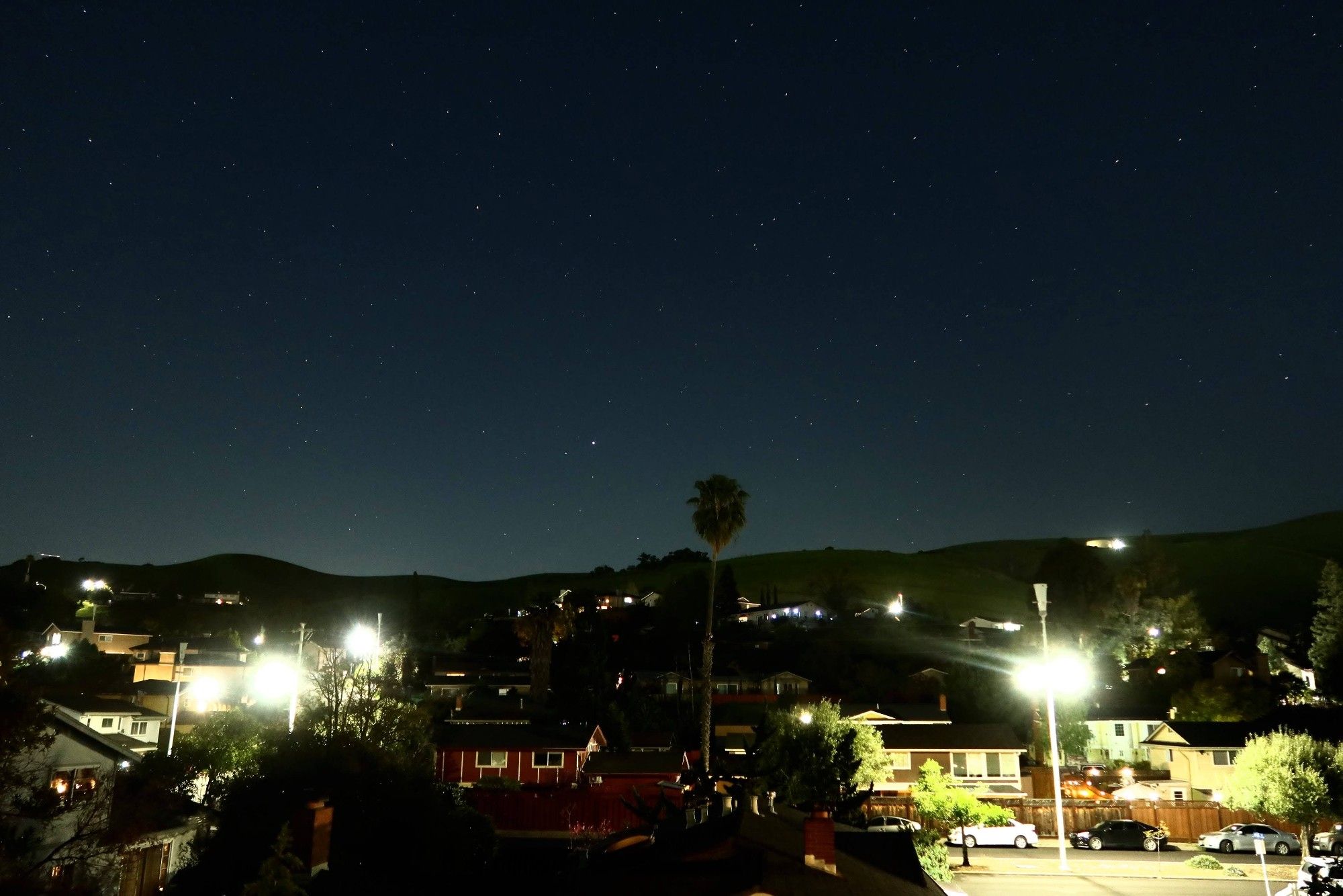 Starry night sky with a brightly lit residential area below.