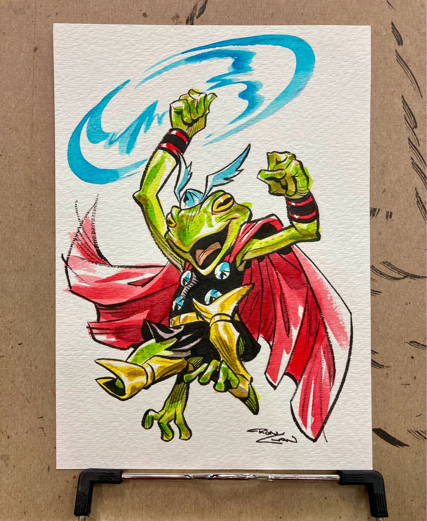 Watercolor art of Frog Thor. He's a green frog with the iconic armor of Marvel's Thor. He jumps through the air swinging his hammer above him in a blue blur.