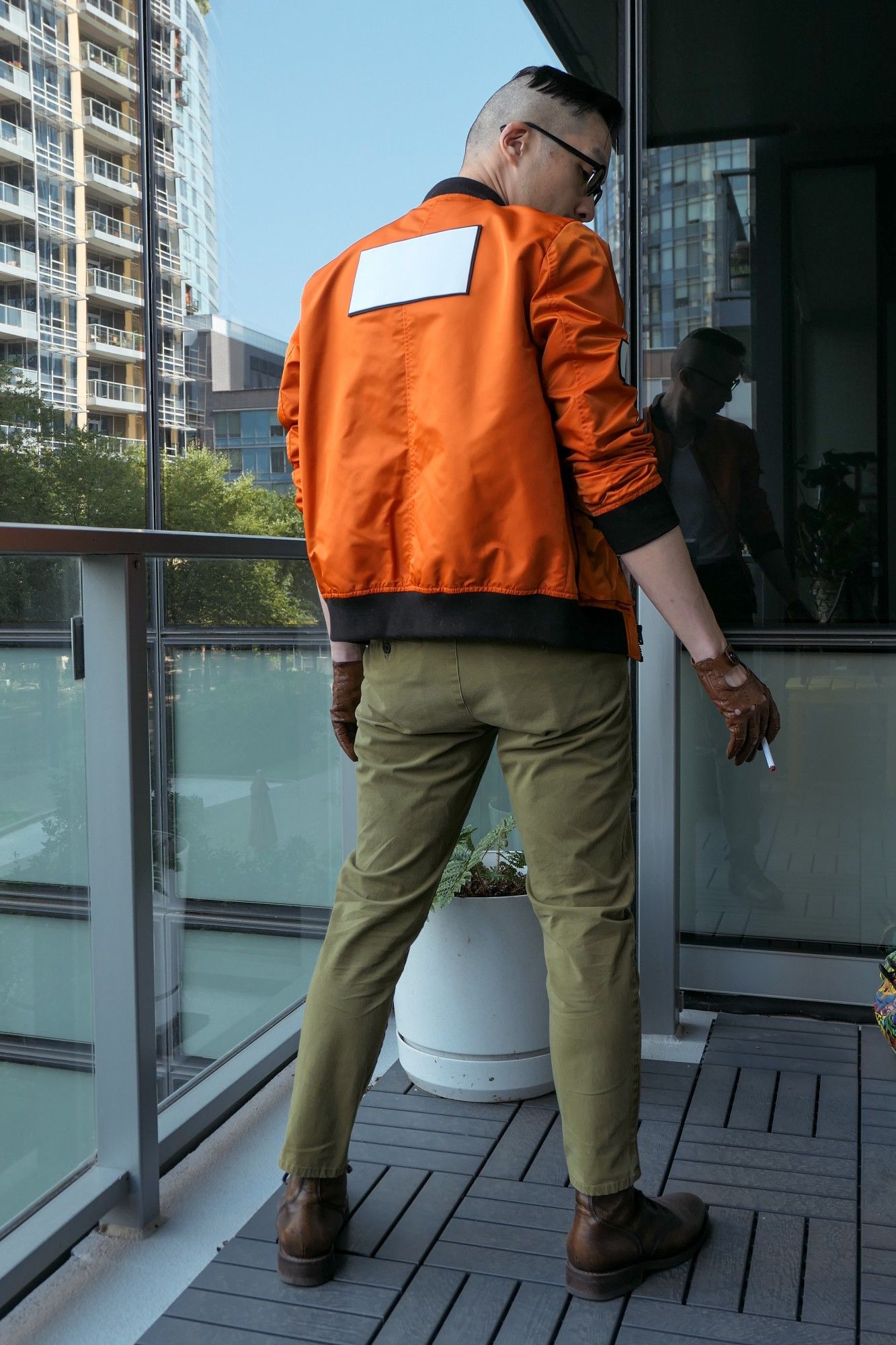 Photo of me dressed as Kim Kitsuragi from Disco Elysium. I'm a middle-aged Asian guy in an orange bomber jacket, olive pants, round glasses, and brown leather driving gloves. Full-figure shot from behind. You can see the jacket has a large white patch across the back.