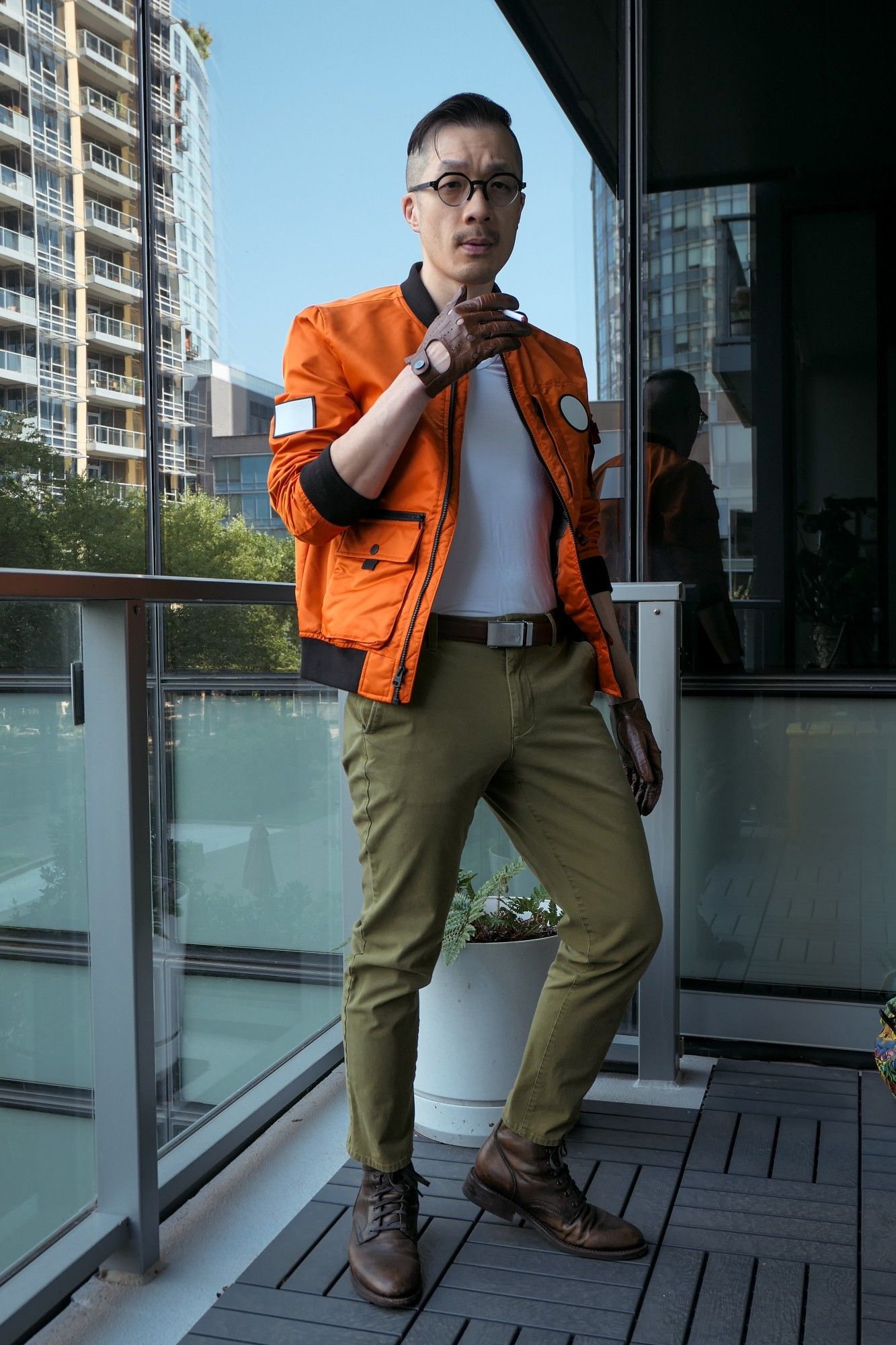 Photo of me dressed as Kim Kitsuragi from Disco Elysium. I'm a middle-aged Asian guy in an orange bomber jacket, olive pants, round glasses, and brown leather driving gloves. Full-figure shot, I'm holding a fake cigarette.