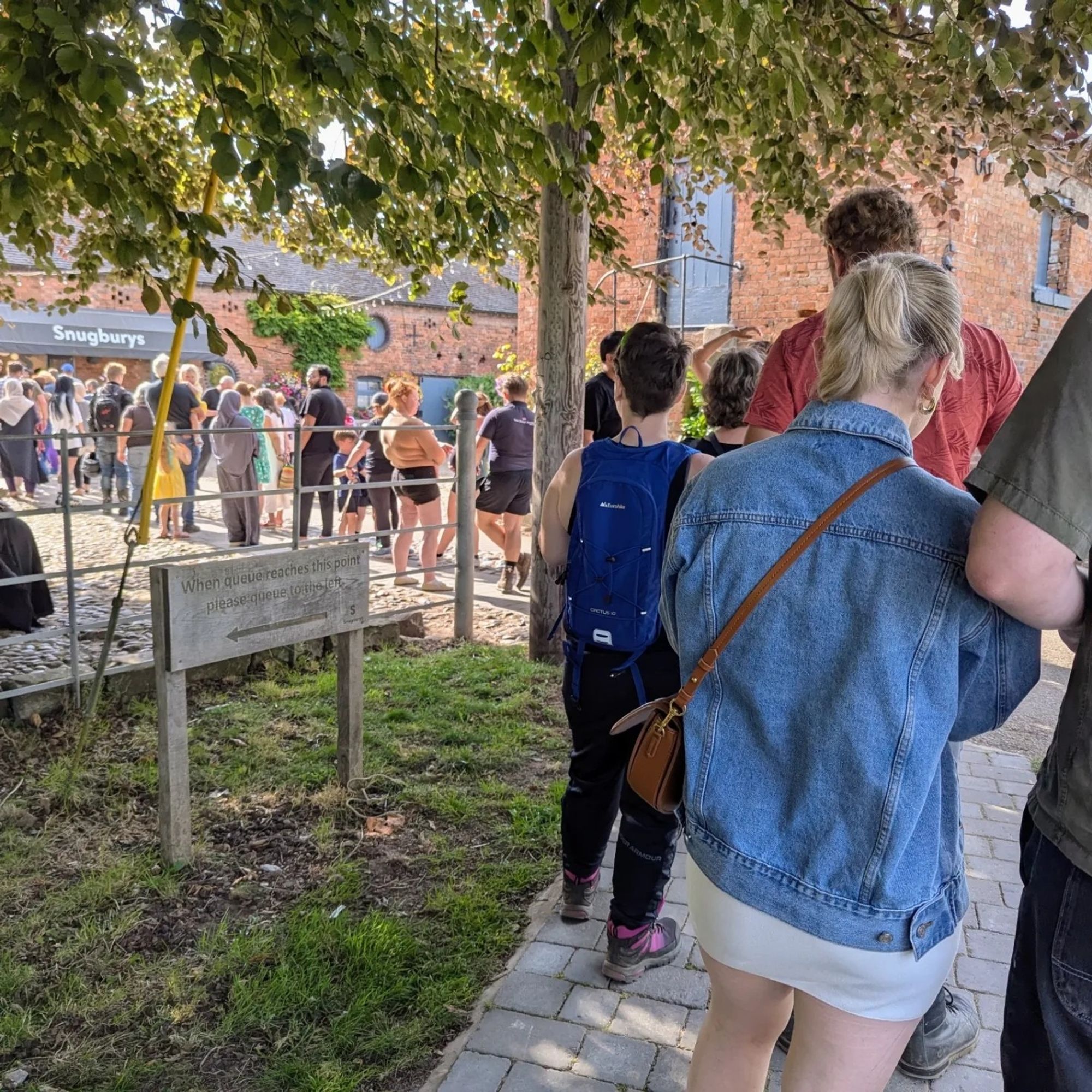 A long queue of people patiently waiting for ice cream in the courtyard in front of farm buildings