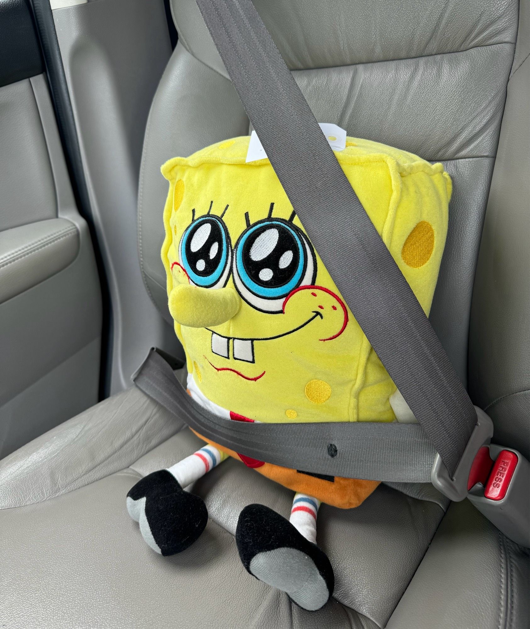 A large SpongeBob plush doll buckled into the front seat of a car