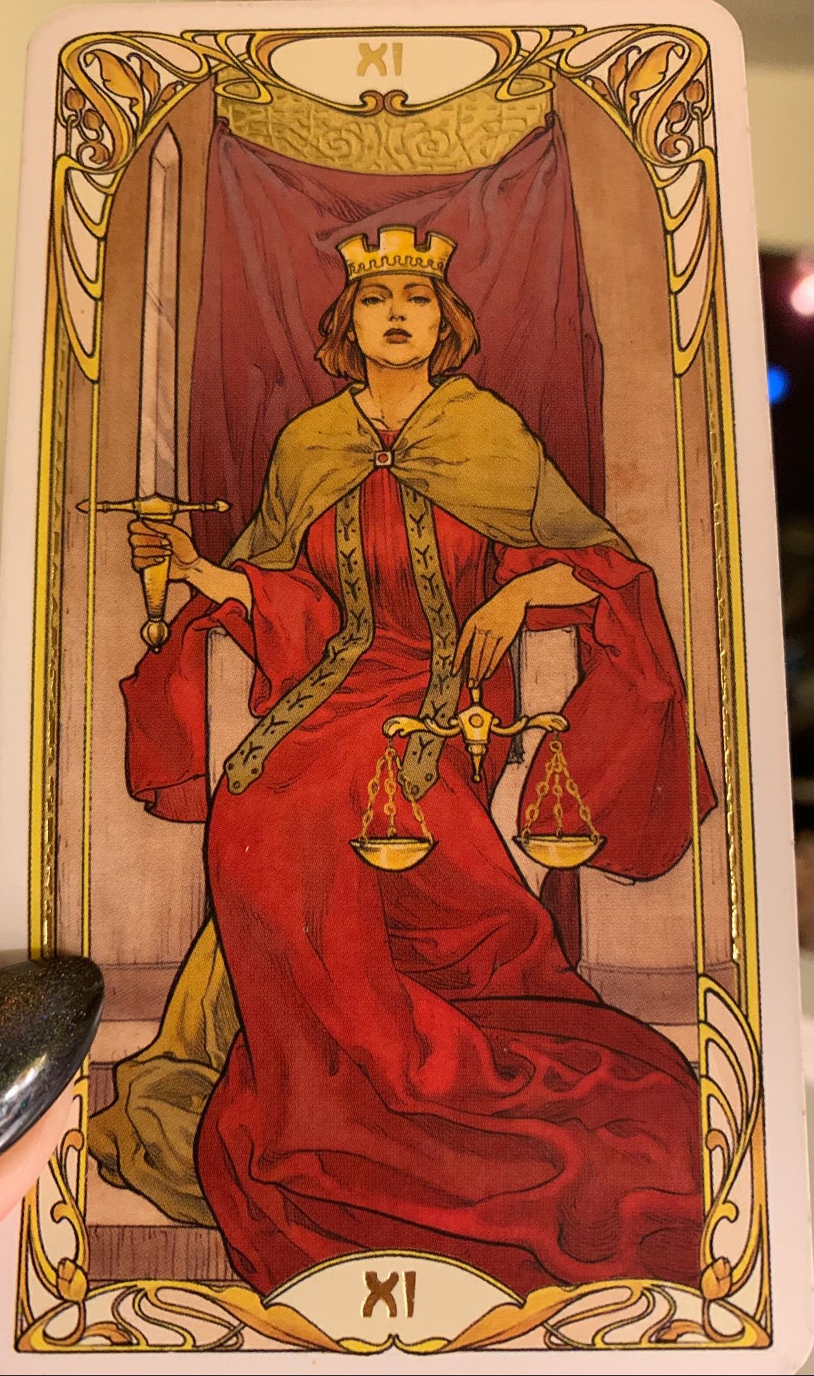 Justice, Major Arcana 11, from the Golden Art Nouveau tarot deck. It shows a crowned woman sitting on a throne, wearing a crimson dress edged in gold. She is holding a sword in her right hand and a pair of scales in her left. The scales are balanced.