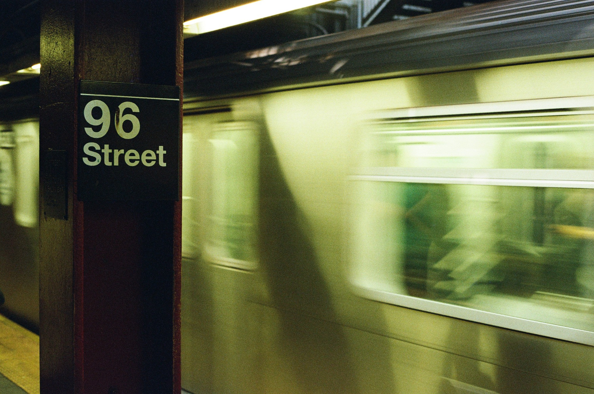 A subway train passing by a 96th Street sign.