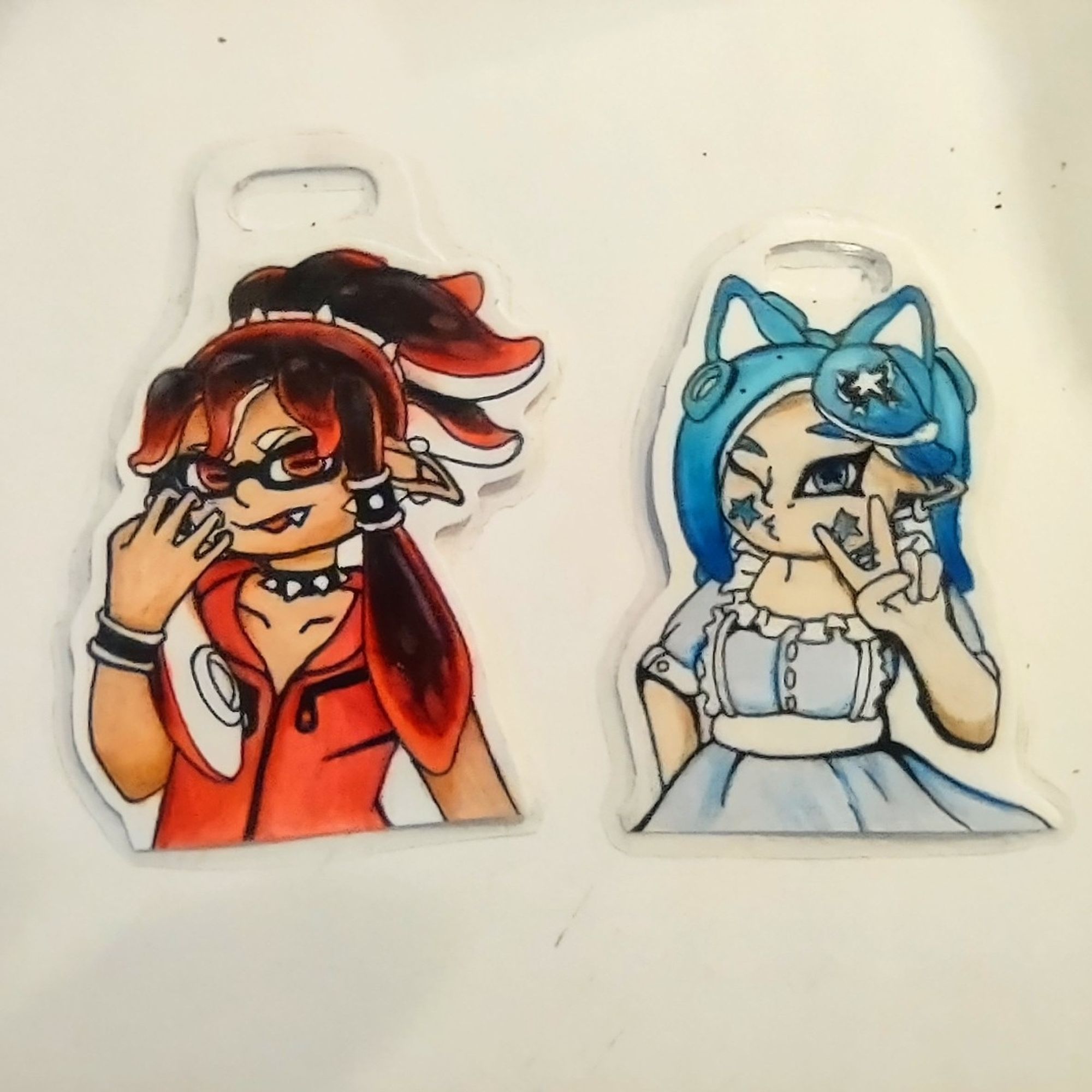 Image of two original characters from the game splatoon on a white background. One has blue tentacle like hair the other has black tentacle hair with red at the tips. The blue on is dressed in lolita style light blue dress the other is wearing a red sleeveless zip up hoodie and punk spiky jewelry.