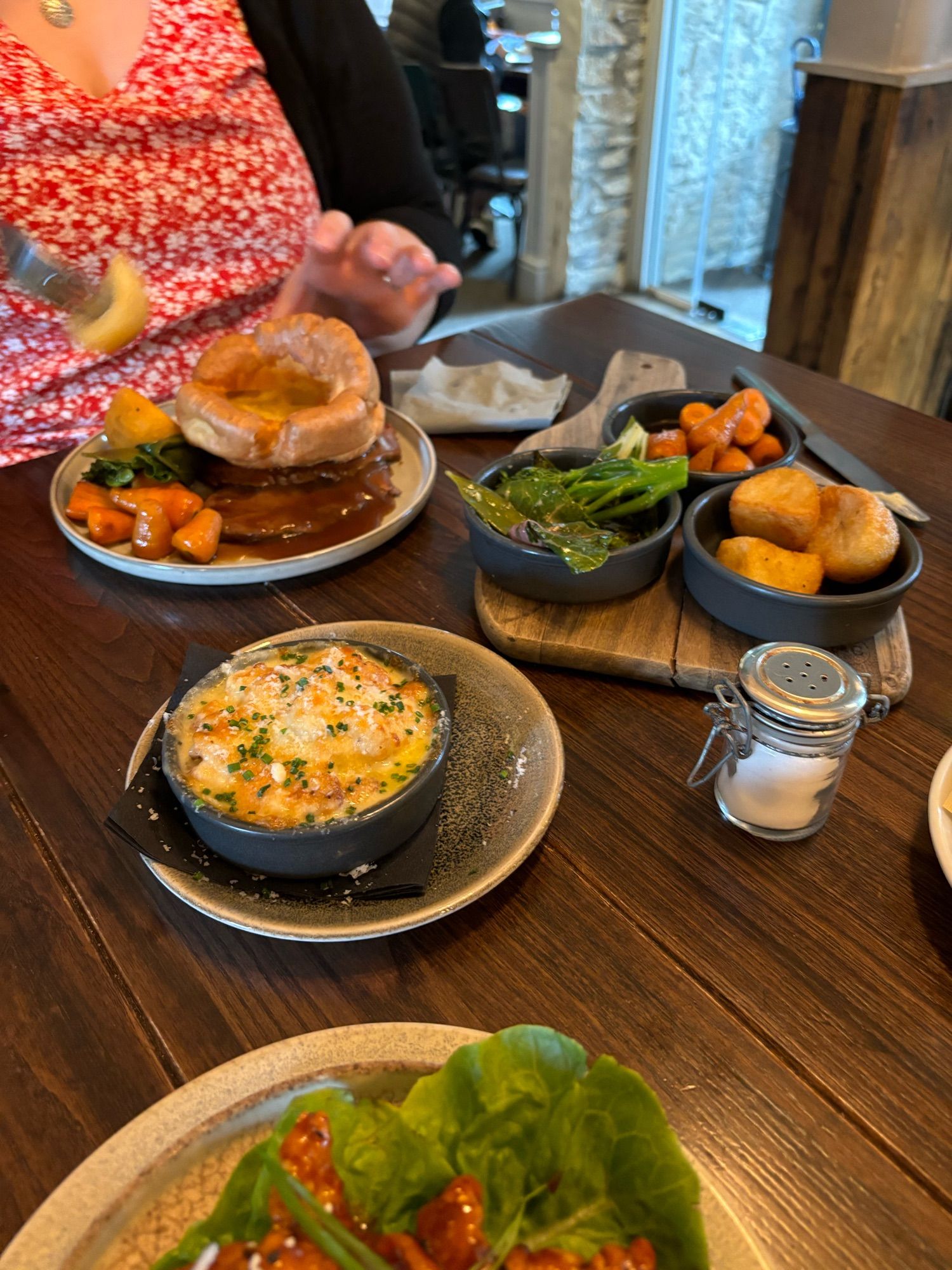 A selection of plates with beef, Yorkshire pudding, roast potatoes, cauliflower cheese, maple & orange roasted carrots, and some buttered greens.