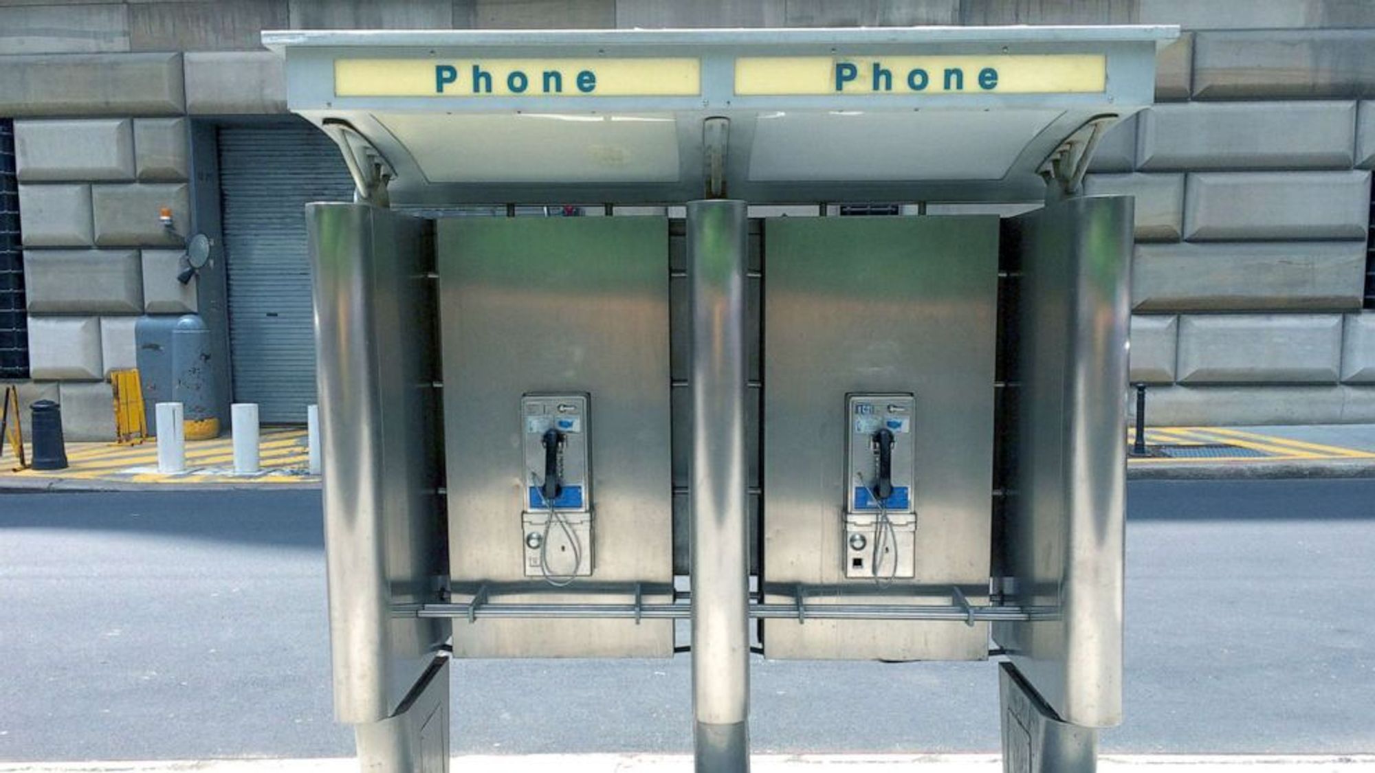 block of two new york city payphones sturdily enclosed in a large metal structure anchored into the concrete