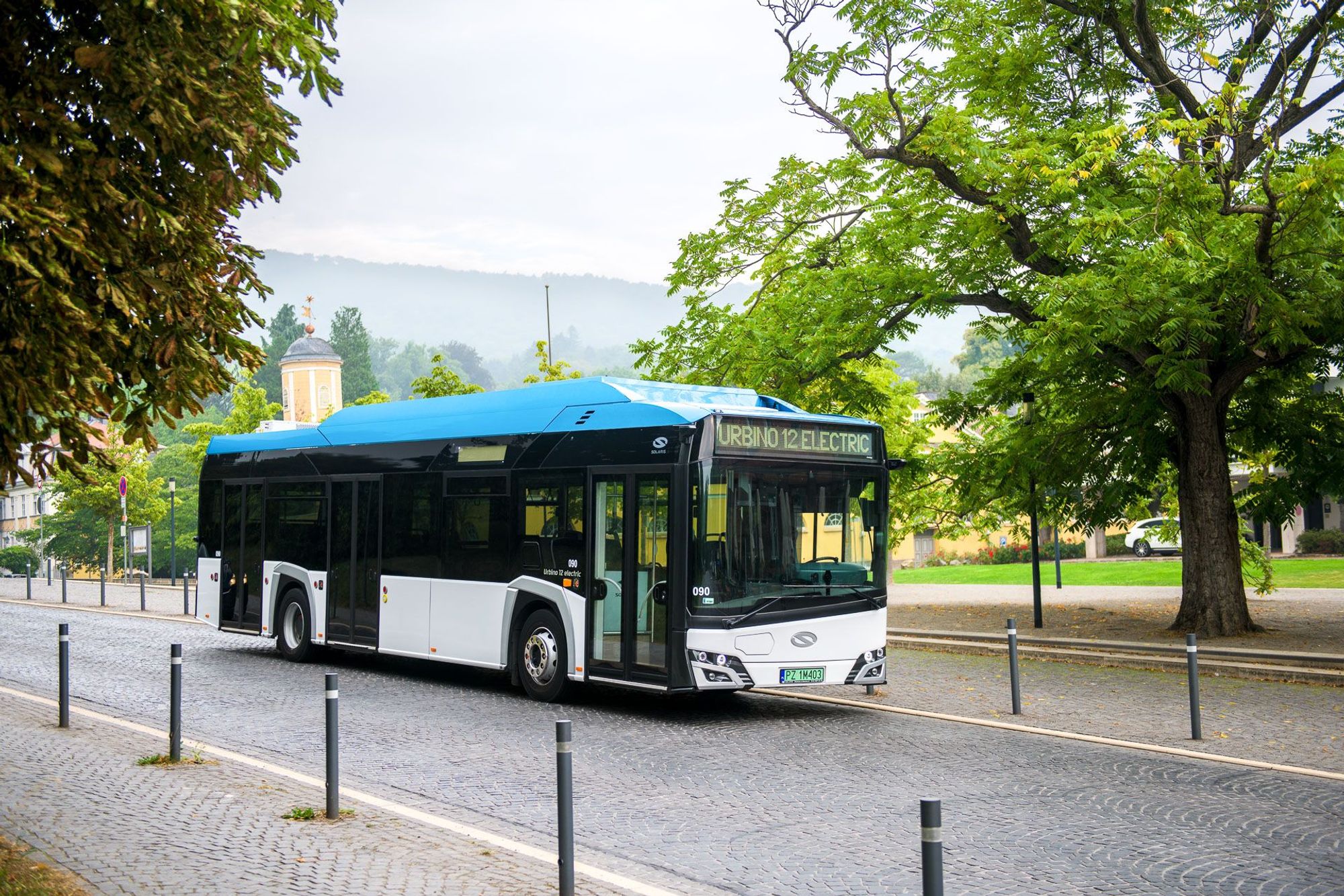 Electric bus on a cobblestone street beside green trees.

Photo by Solaris