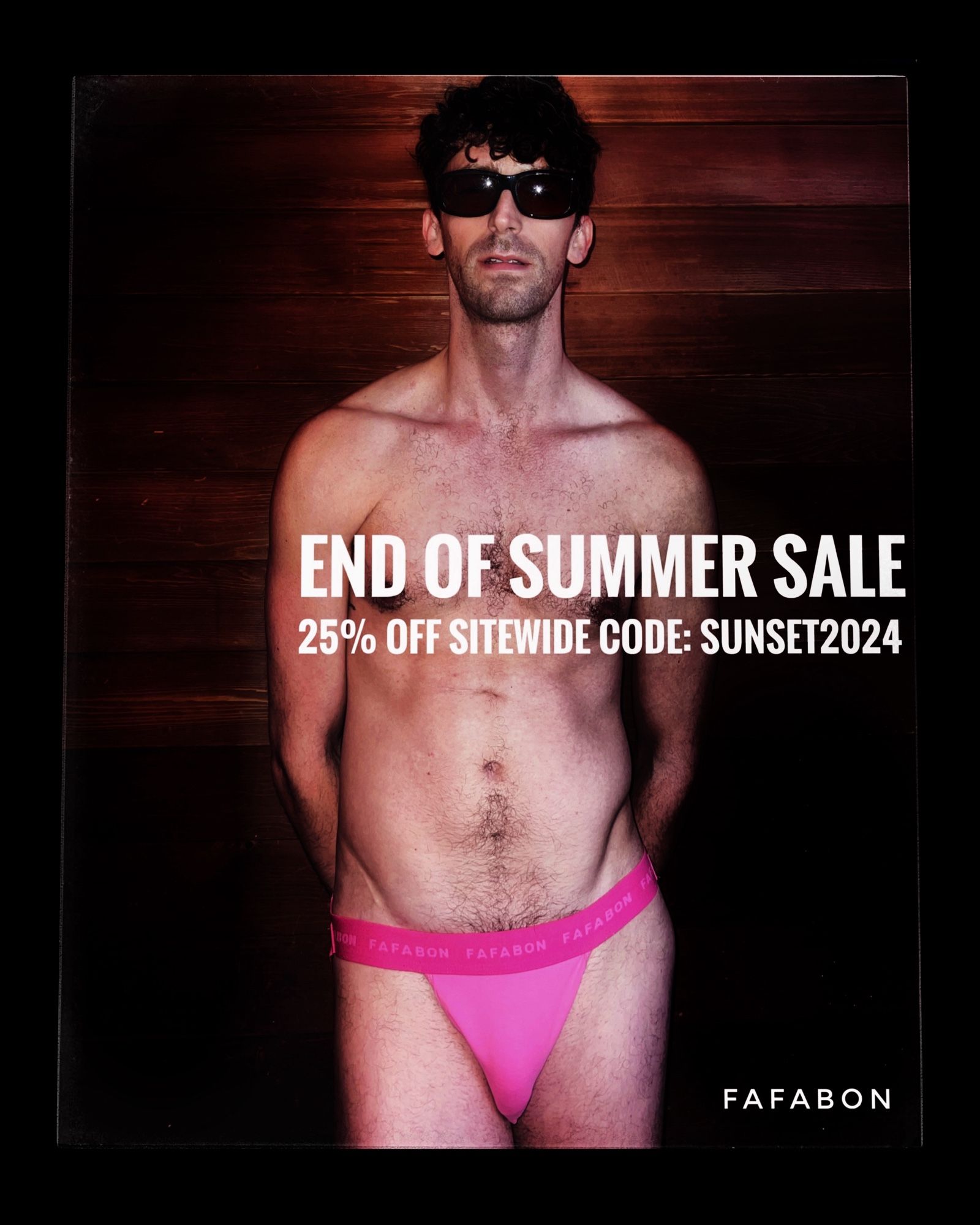 model standing in front of wooden wall in pink jockstrap and sunglasses.