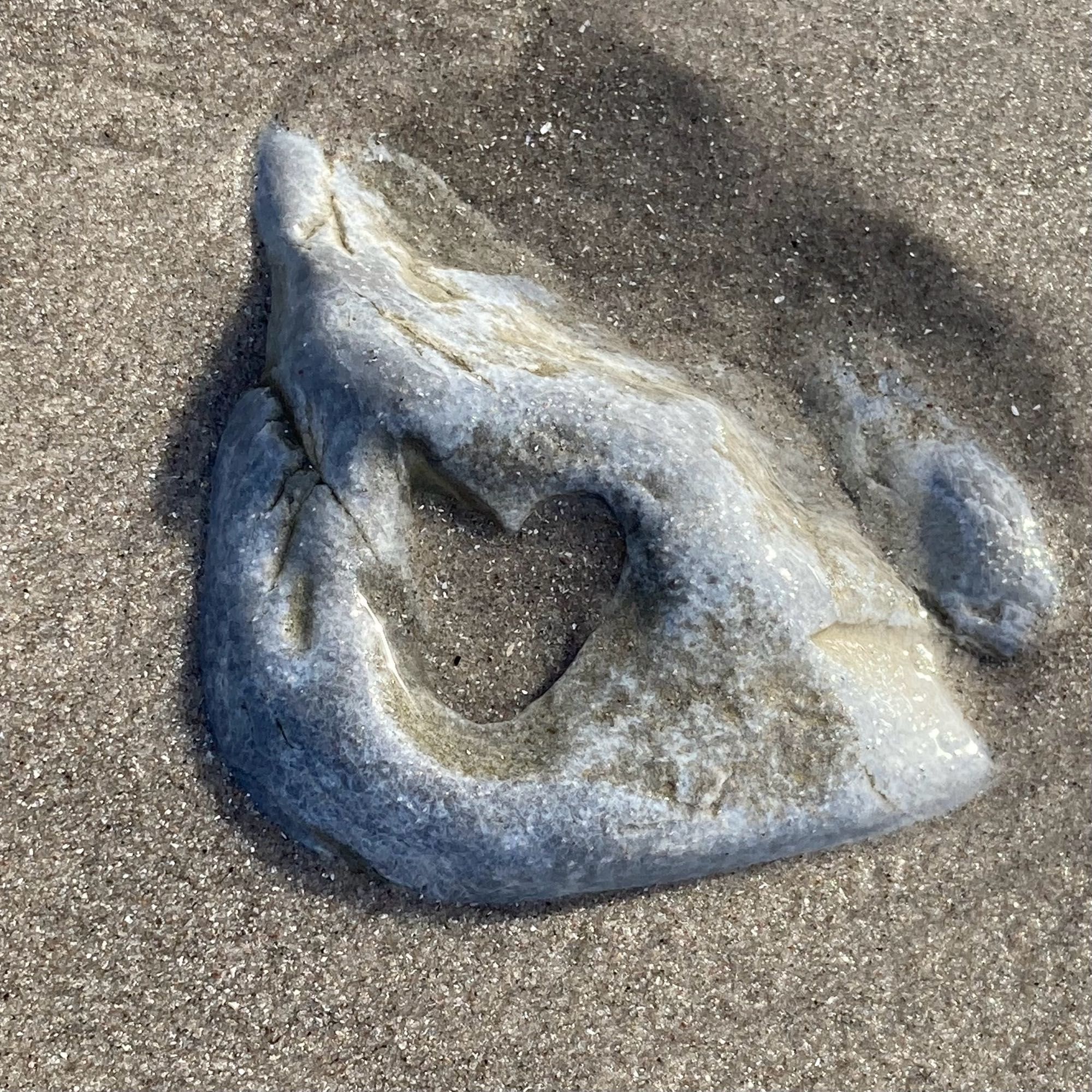 ein großer stein liegt im strandsand, innen ist er ausgespült in form eines herzens