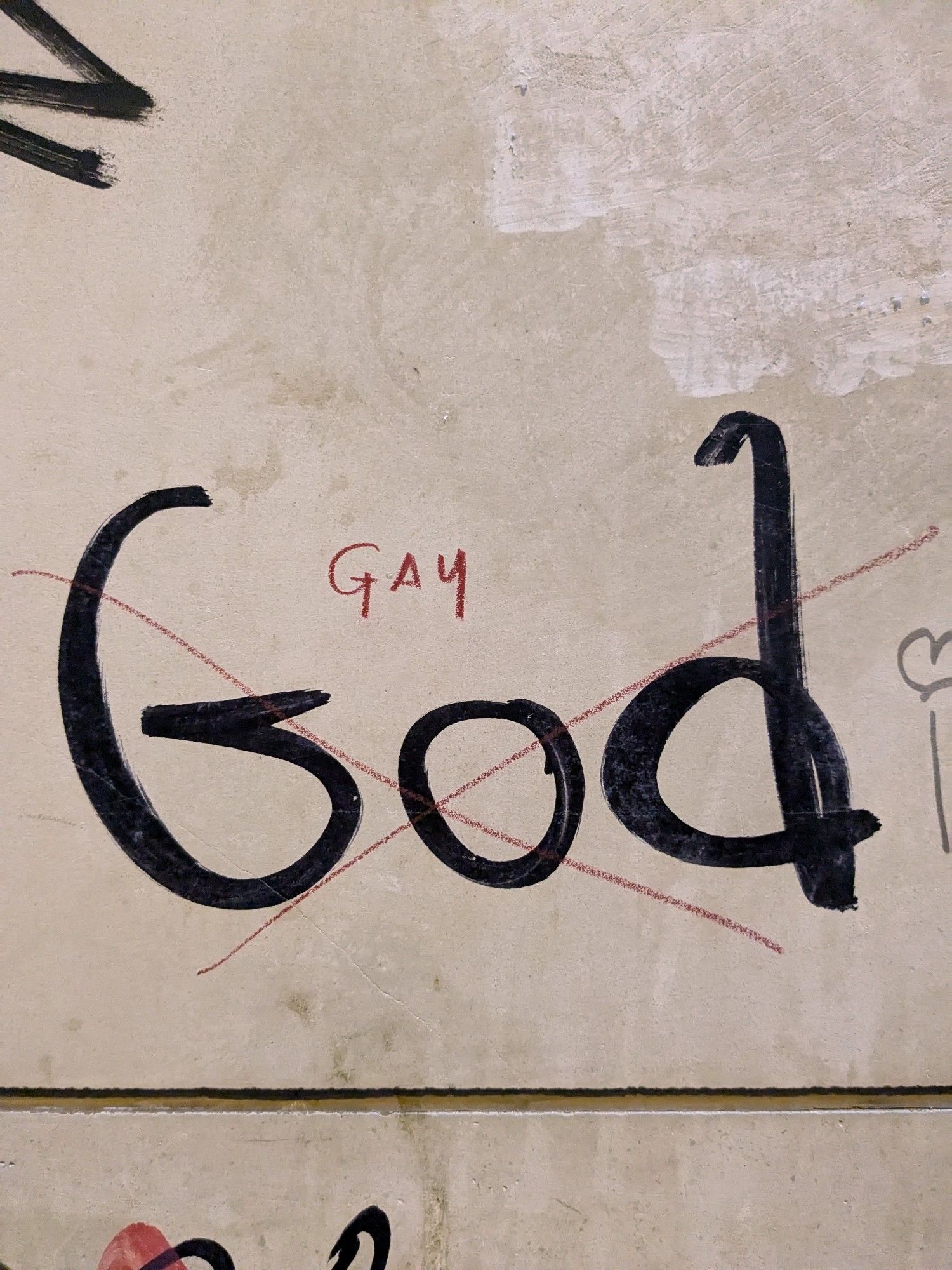 God written on a wall but it has been crossed out with eyeliner and replaced with "gay"