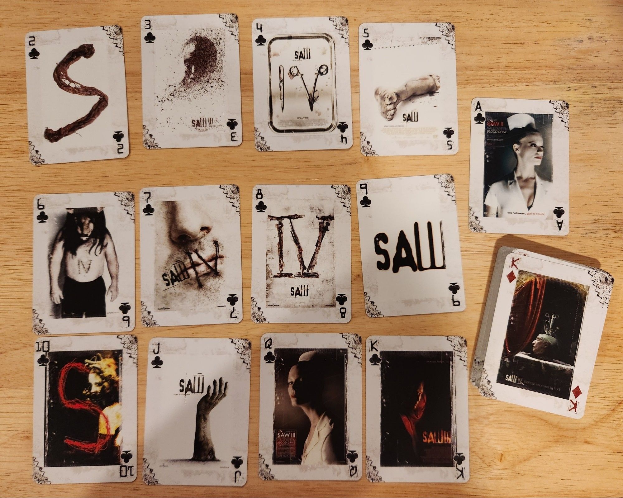 A photograph of the set of Clubs from a deck of promotional Saw playing cards. The faces of the cards each contain a poster design or piece of artwork from the marketing campaigns from one of the first four Saw movies.