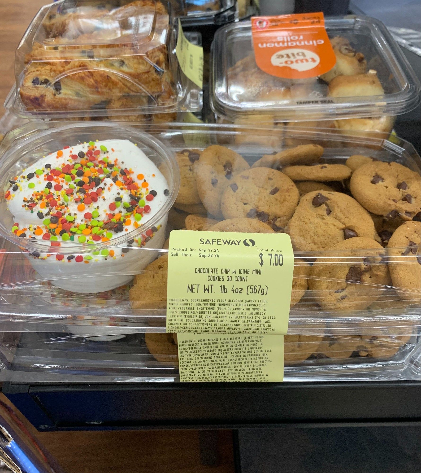 30 chocolate chip cookies for sale with a pint of white icing topped with sprinkles.