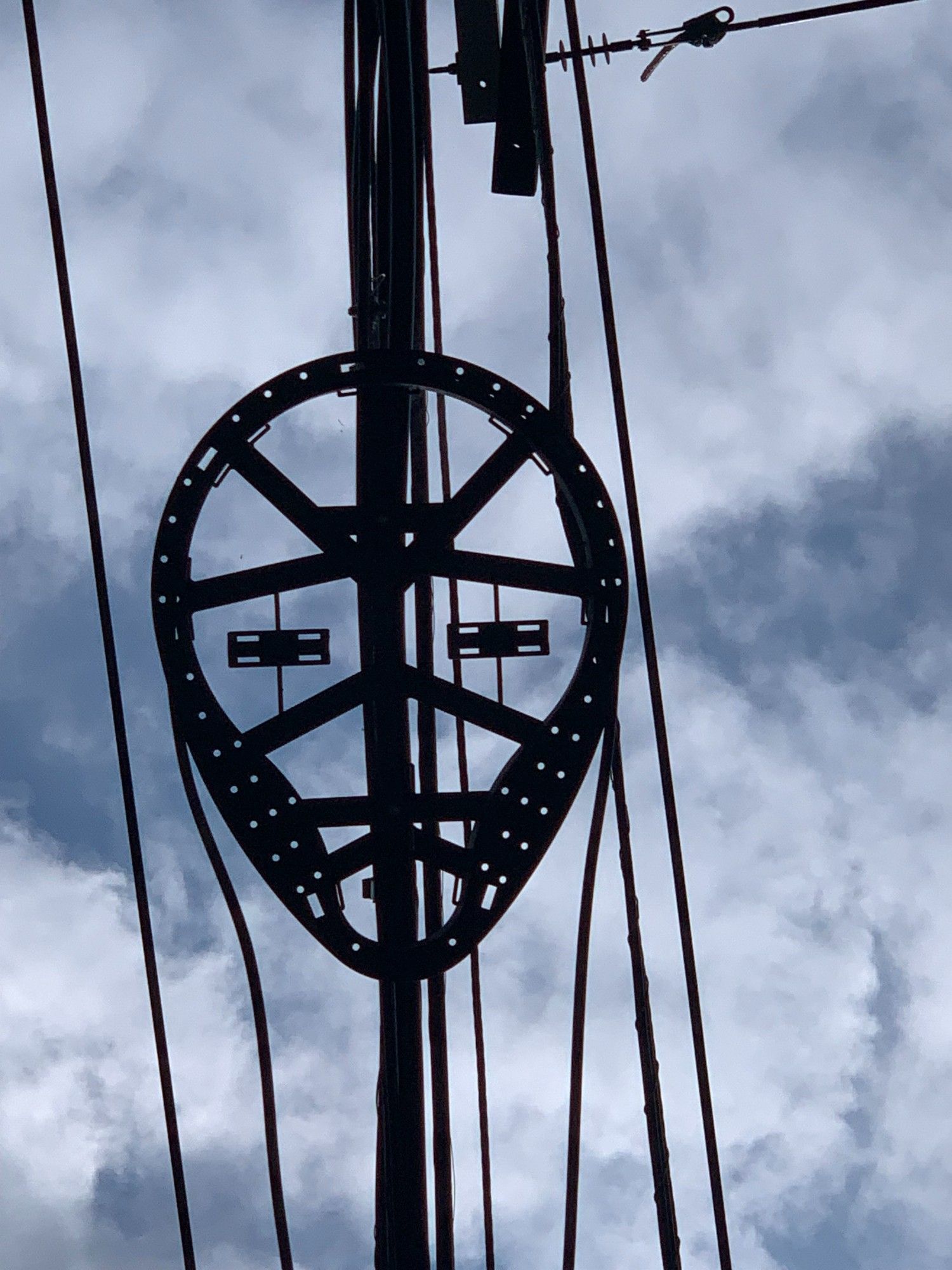 Close-up of a telephone and power line array that looks like it could be a mask for a human face. Thin clouds are in the background of the picture, taken from the ground looking up.