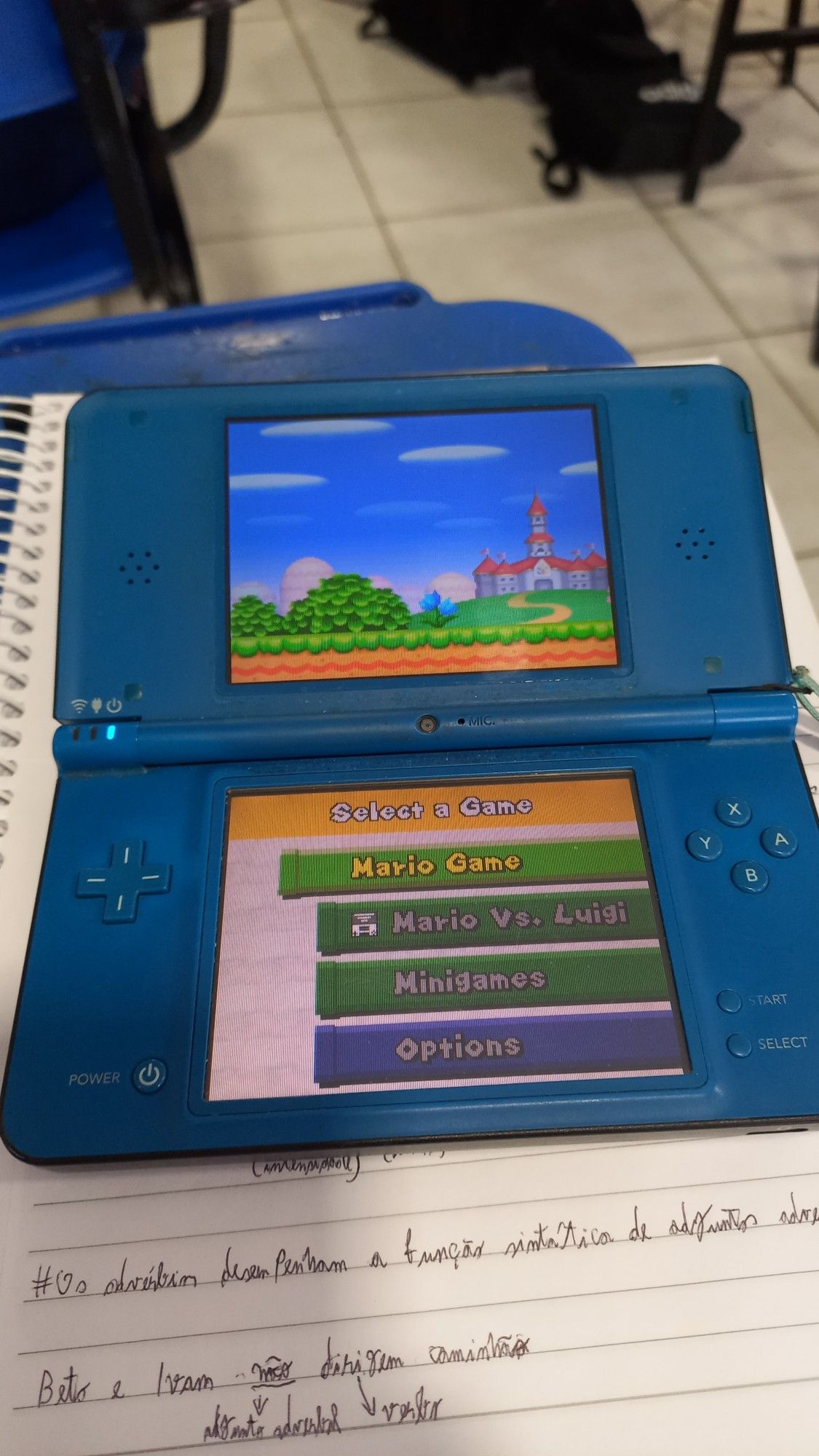 Um nintendo ds xl azul encima de um caderno em uma sala de aula