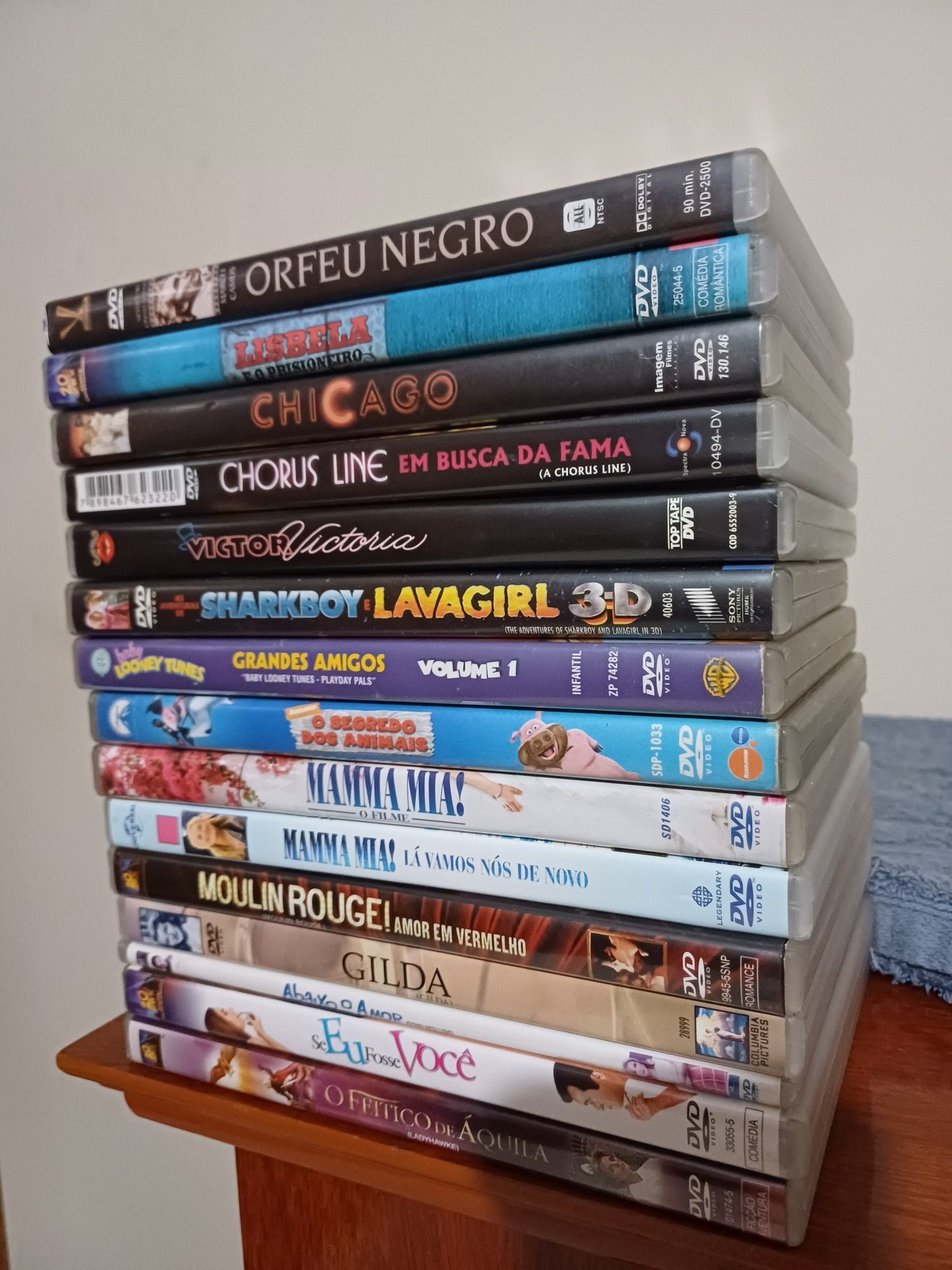 Uma pilha de DVDs contendo os seguintes filmes: orfeu negro, lisbela e o prisioneiro, chicago, a chorus line, victor/victoria, sharkboy e lavagirl, baby looney tunes volume 1, o segredo dos animais, mamma mia, mamma mia: lá vamos nós de novo, moulin rouge, gilda, abaixo o amor, se eu fosse você e o feitiço de áquila