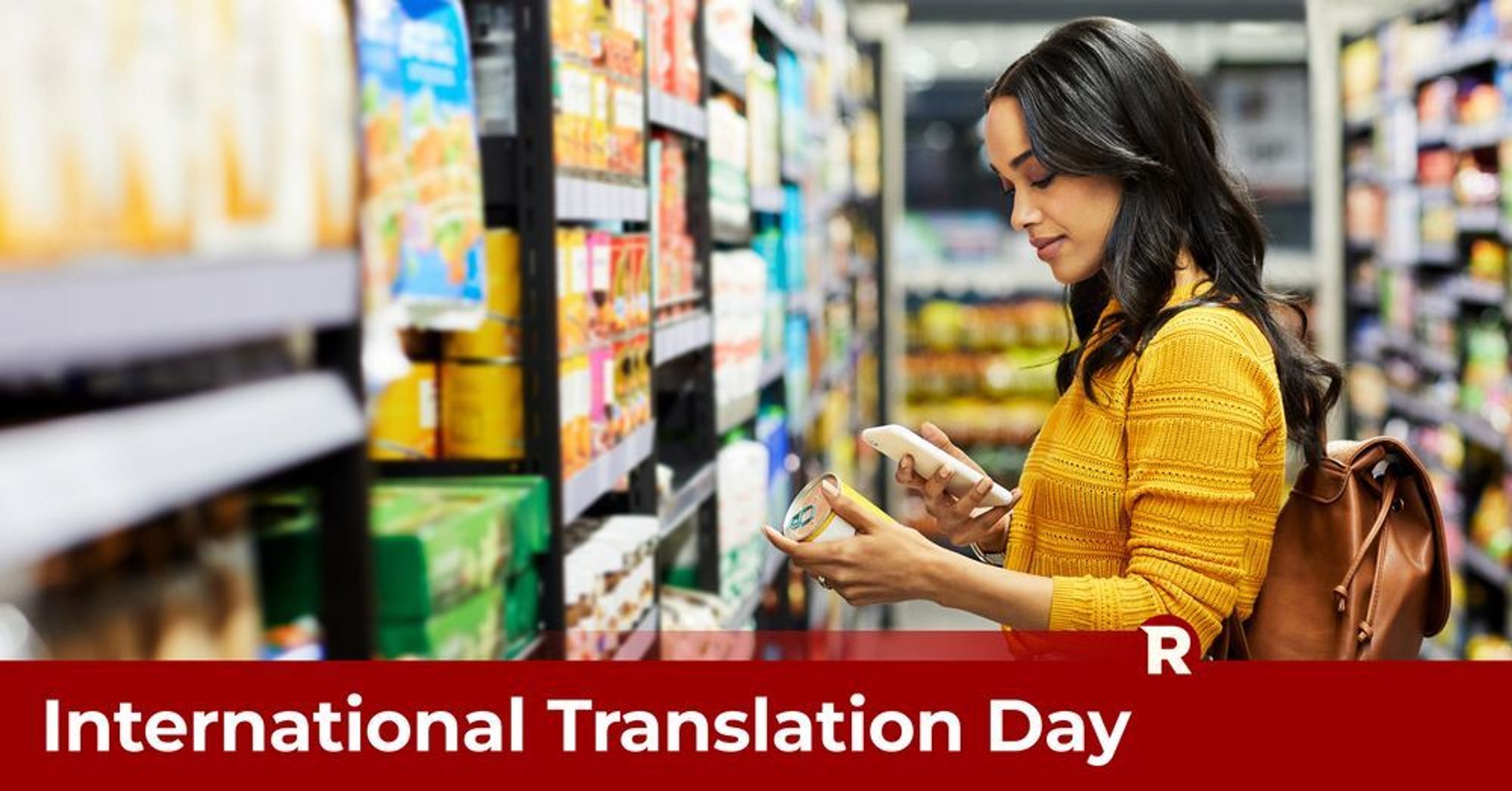 A young woman with long black hair, wearing a yellow cardigan stands in a store looking at food tin label through her phone for translation - International Translation Day