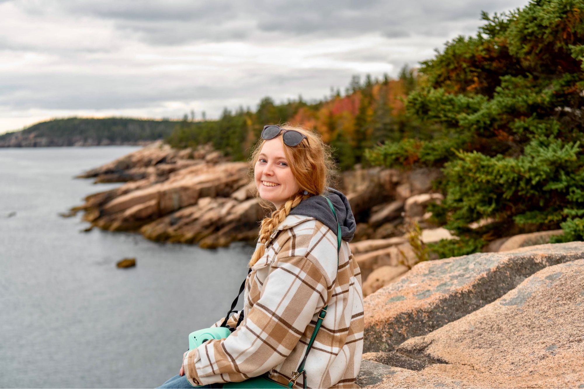 Lillie sitting on a cliff overlooking the water at Acadia National Park on a fall day.