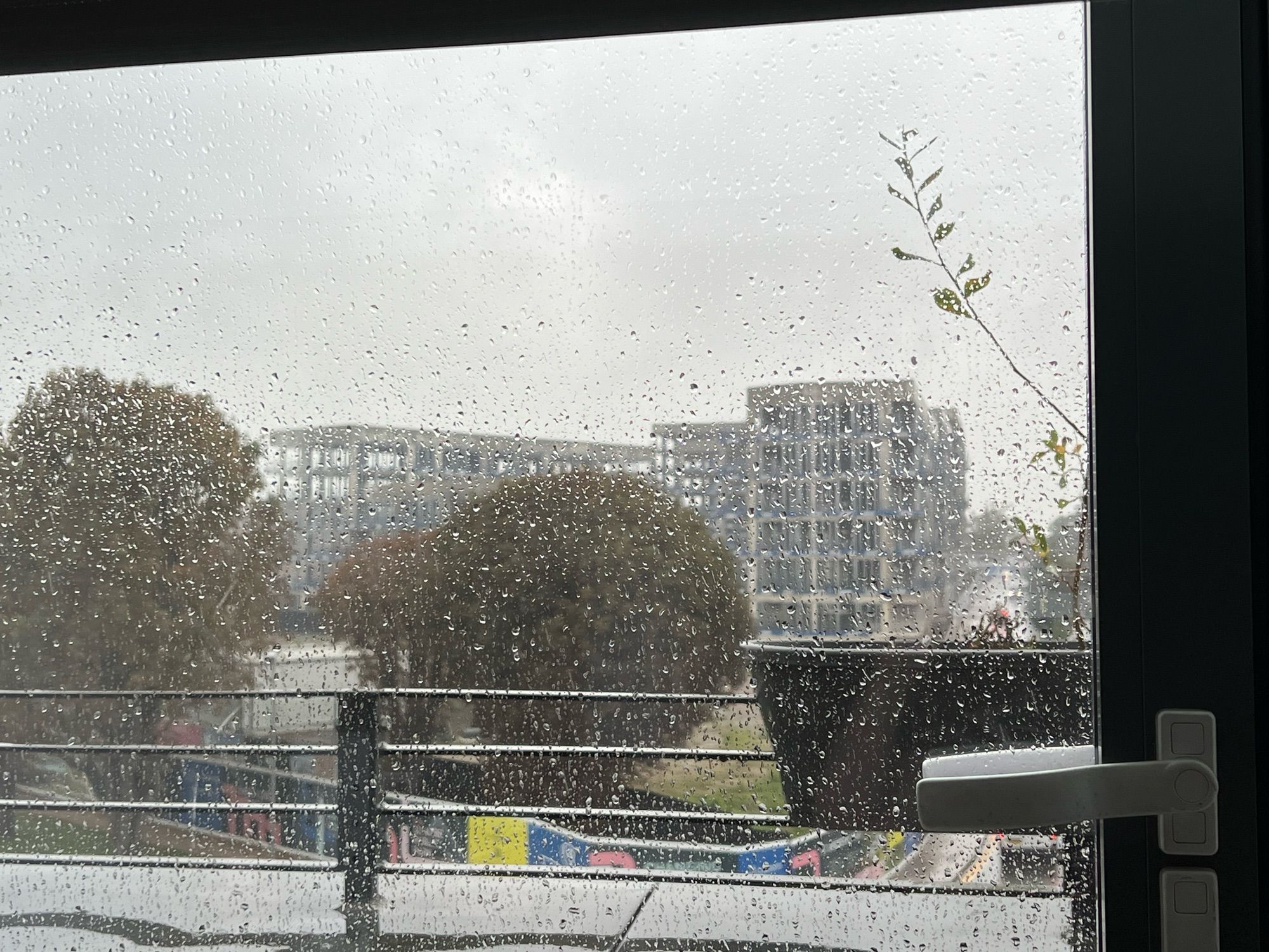 A photo of wet concrete skeletons of buildings. An abandoned construction site. There are trees too, and a road. So basically the same as the other photo, but obscured behind a rain covered window.