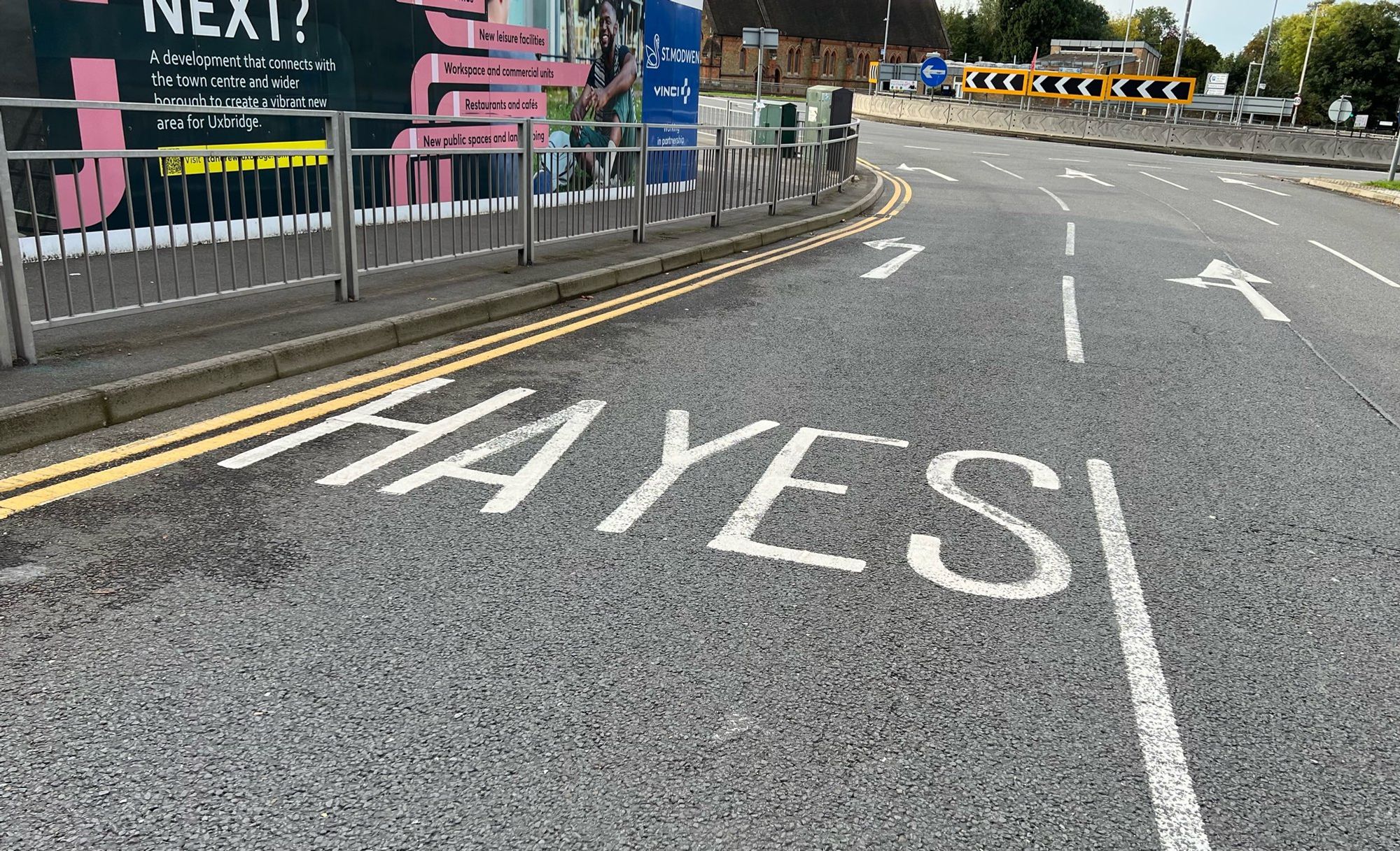 A photo of a left turn lane on approach to a roundabout. It is marked as the turning for the town Hayes, but there is a gap between the a & y, so it appears to read as “HA YES”