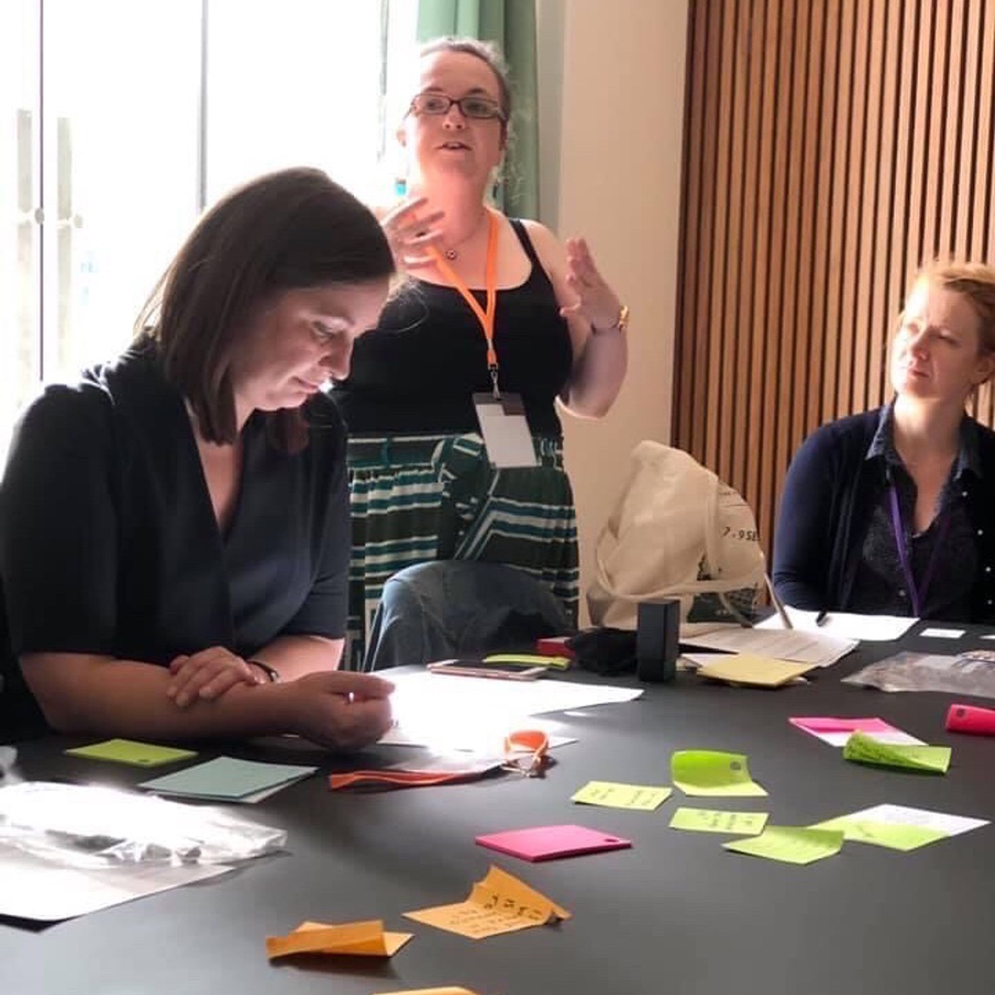 Delivering the workshop - a woman with dark hair in the foreground arrange some post-its and another with blonde hair helps.