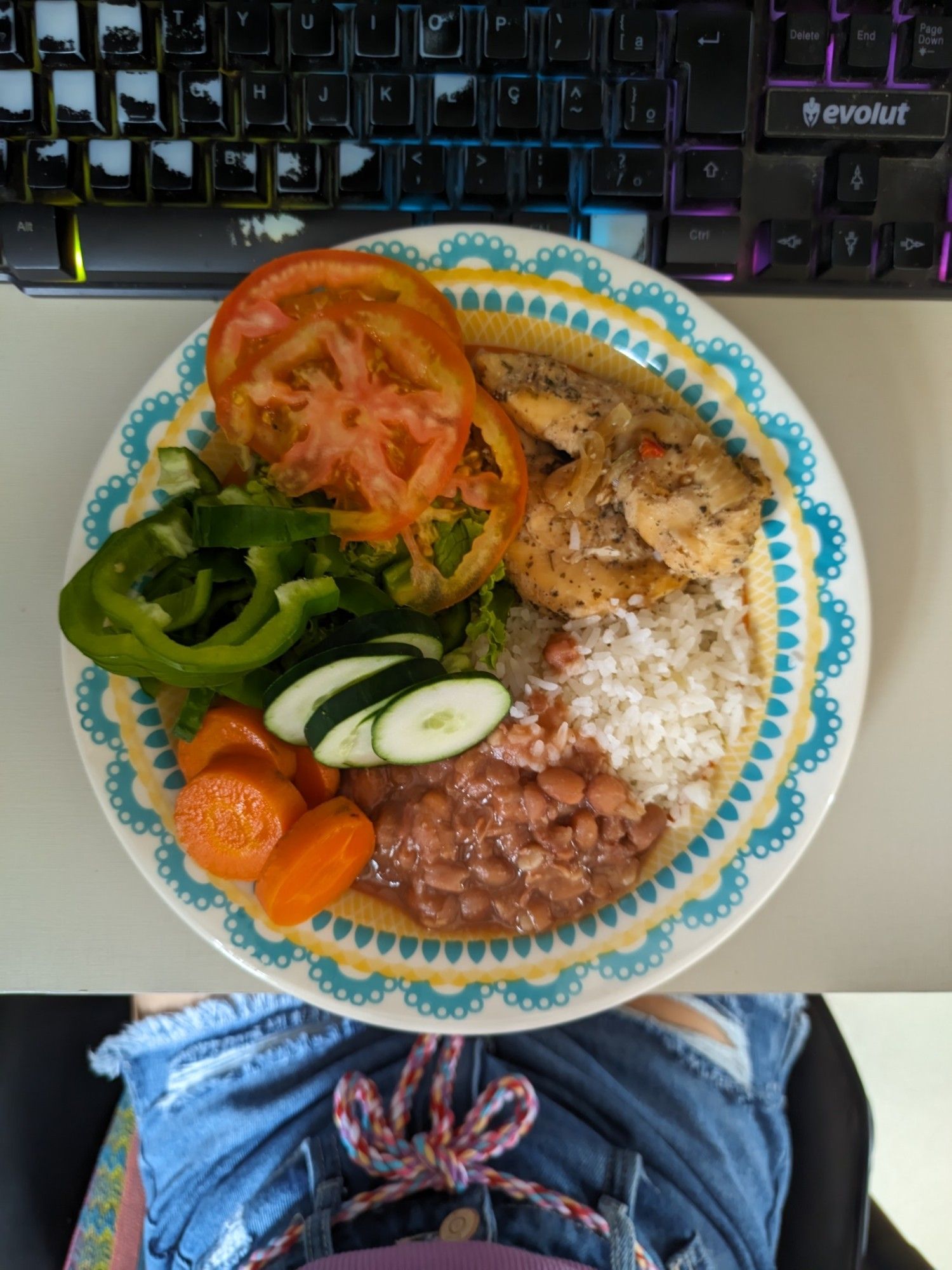 Foto de prato de almoço. A metade esquerda é salada, com alface, rodelas de tomate, pimentão verde picado, rodelas de pepino e rodelas de cenoura cozida. A parte superior da metade direita tem frango sassami levemente acebolado, e o restante é arroz branco com feijão carioca por cima/ao lado.