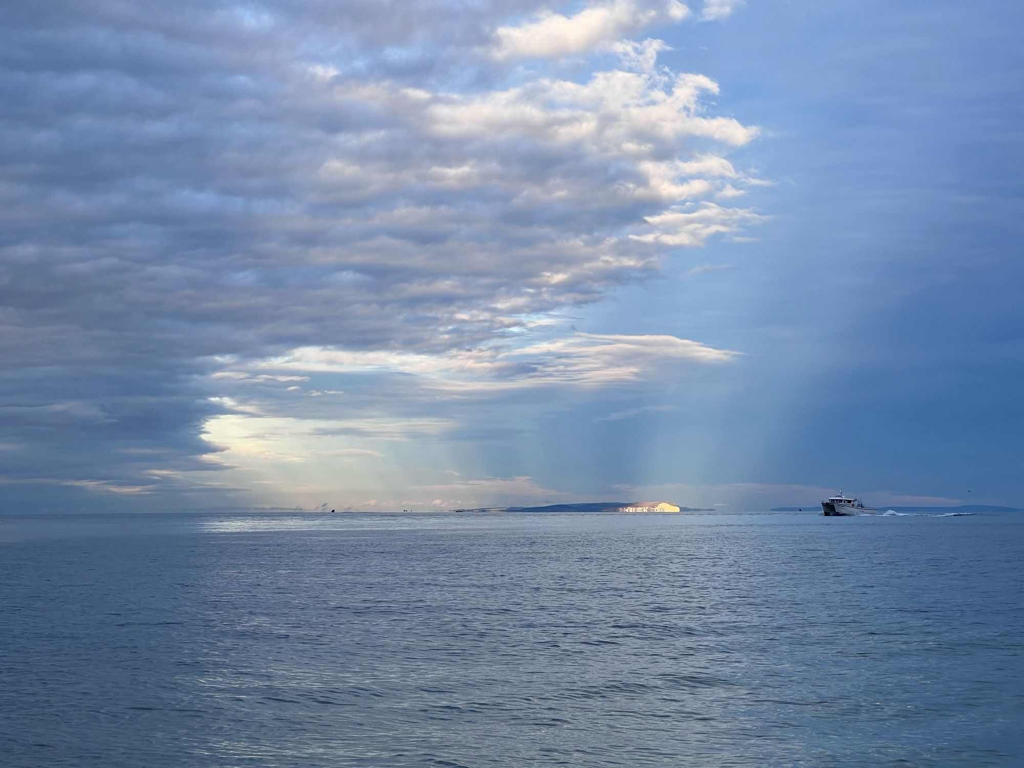 A wider shot of the Isle of Wight with the sun setting behind it and a boat in the foreground