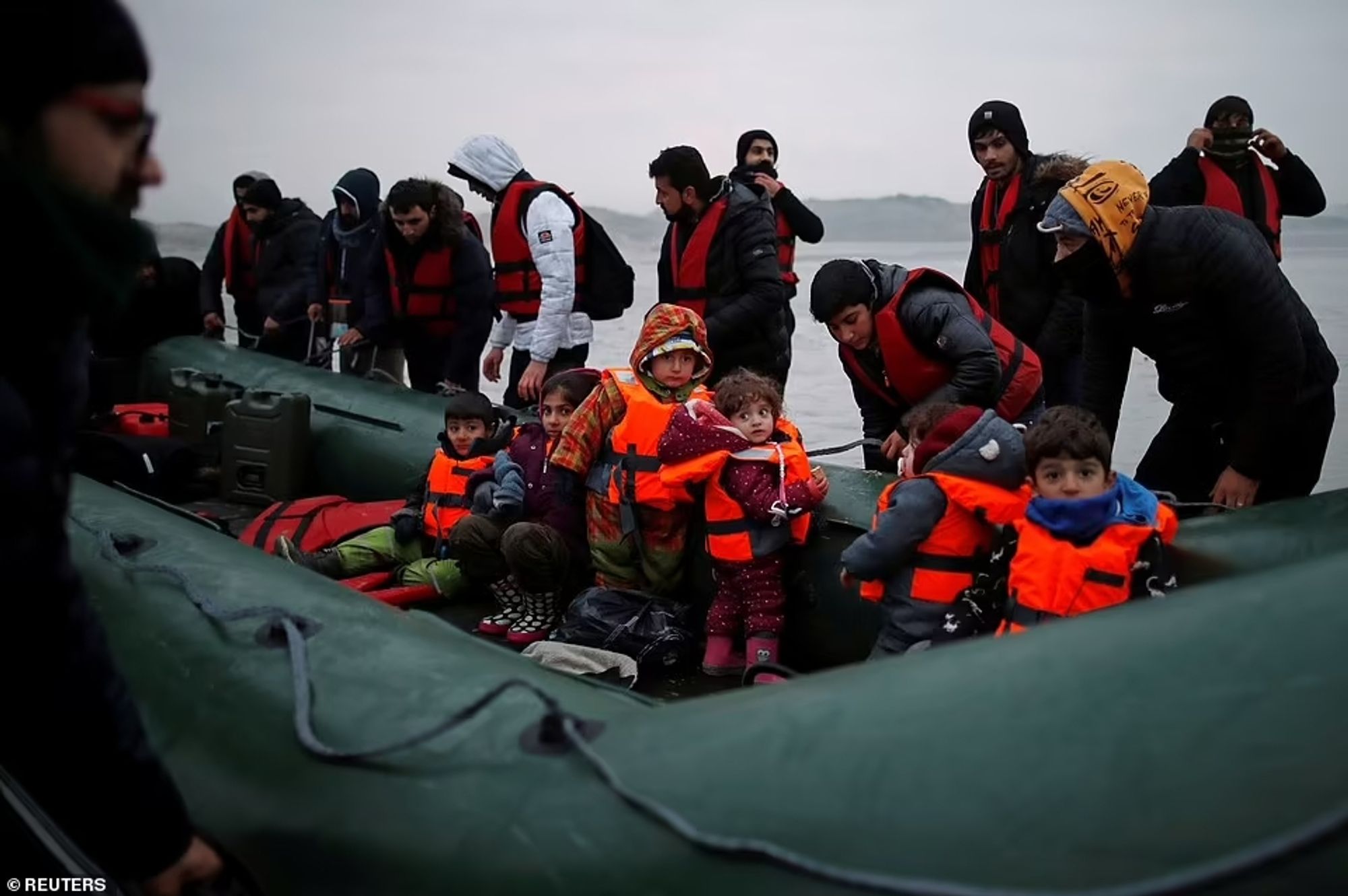 Refugee toddlers and Adults wearing life jackets preparing to embark on a RIB presumably bound for the UK.