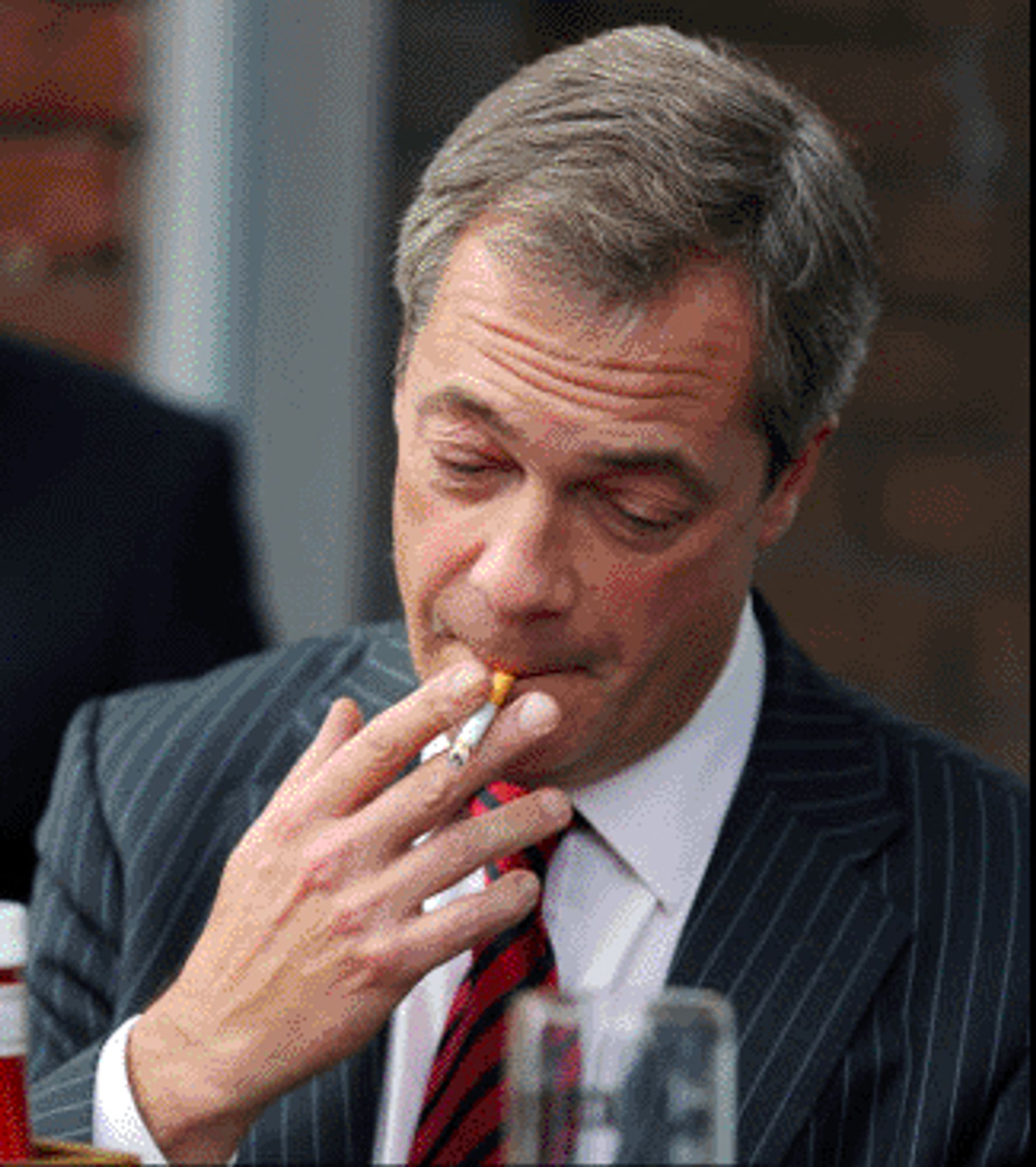 Far right racist leader Farage puffing on the last centimeter of his fag while looking at an empty pint of beer and wishing it was a full glass of wine