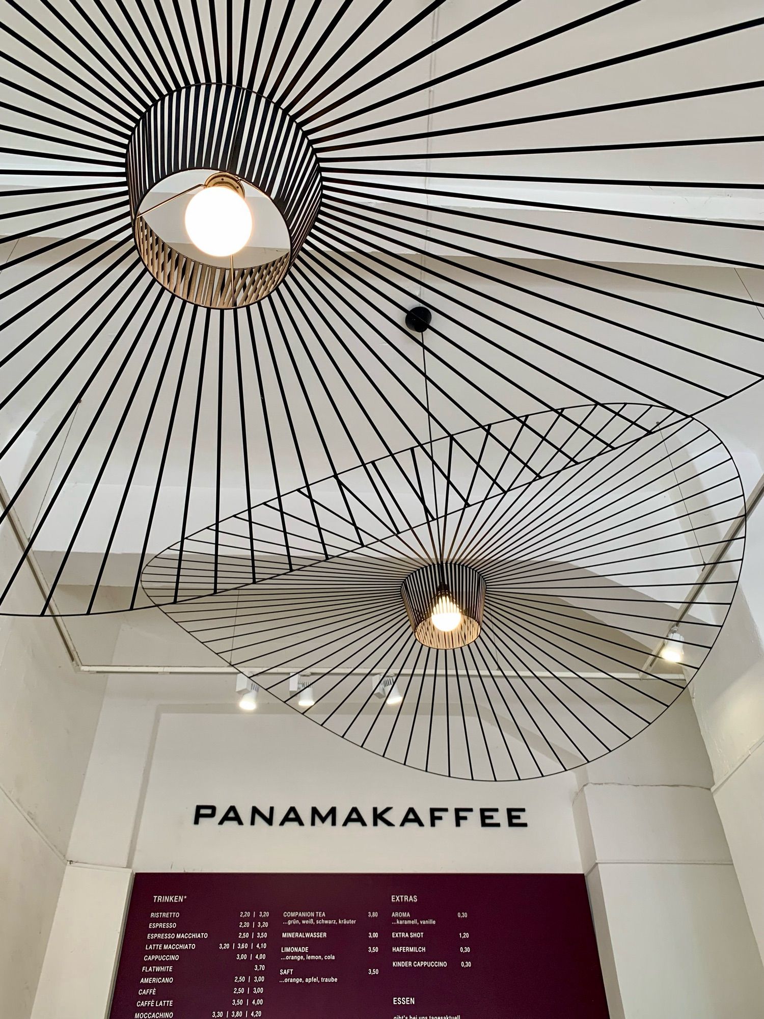 Geometrische Deckenlampen im Panamakaffee, darunter der obere Teil der Preistafel.