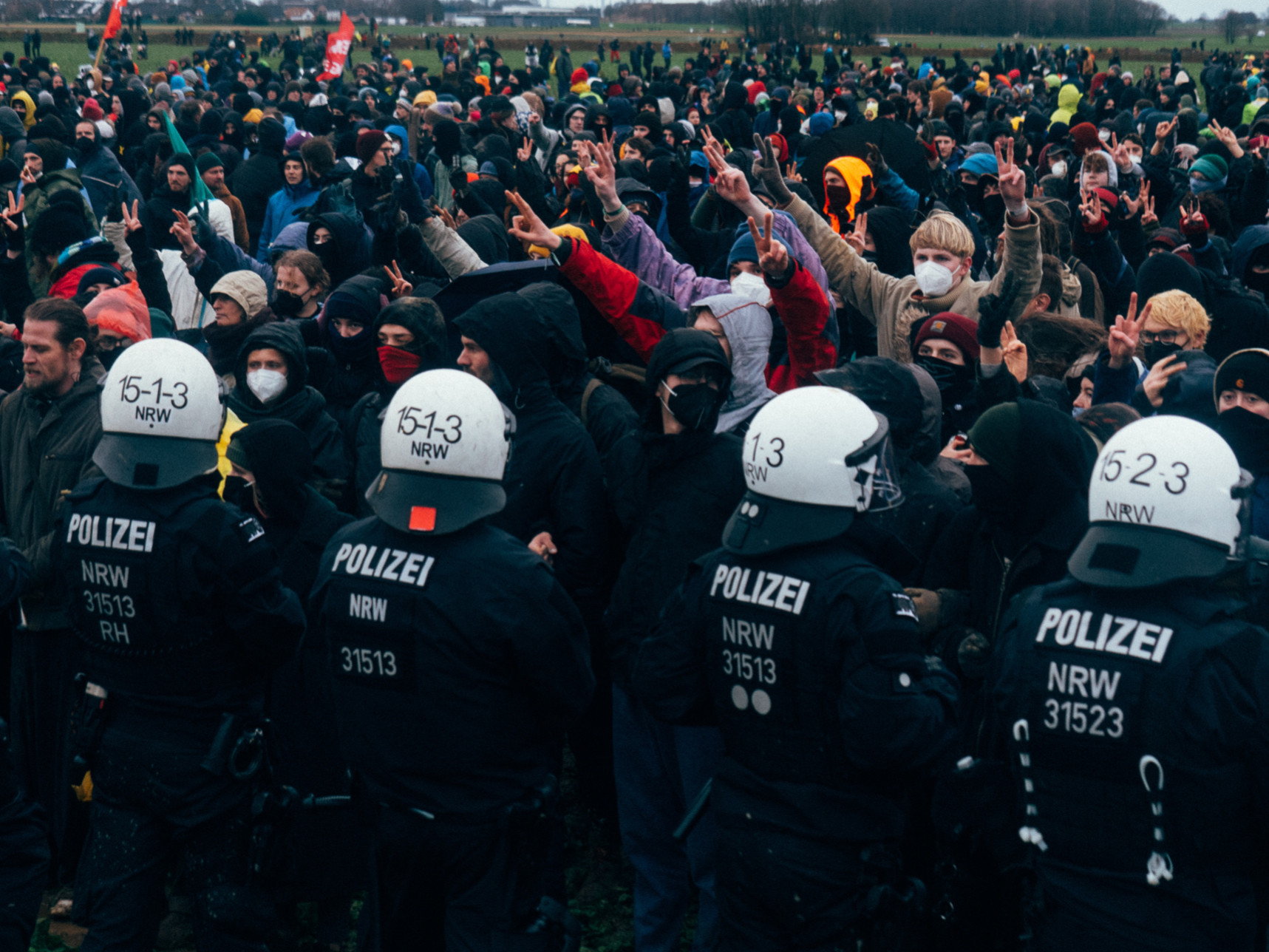 Bild aus Lützerath: 
Meschen stehen vor einer Polizeikette und strecken den Polizist*innen Peace-zeichen entgegen. Bild von der Großdemonstration am 17.01.2023.