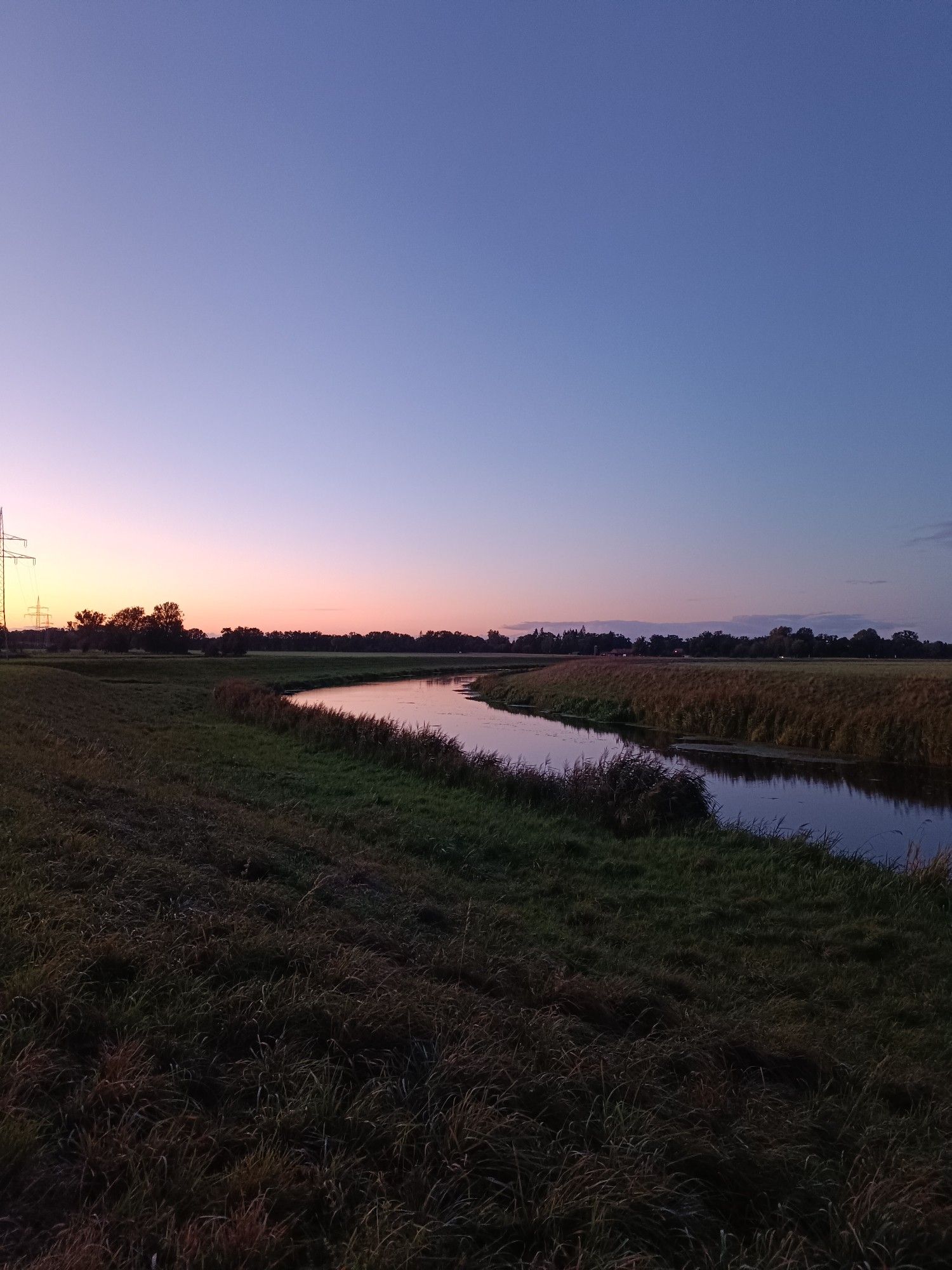 Jeetzelkanal, Kurve, Abendhimmel oben blau unten am Horizont rötlich. Im Vordergrund Gras und Deich.