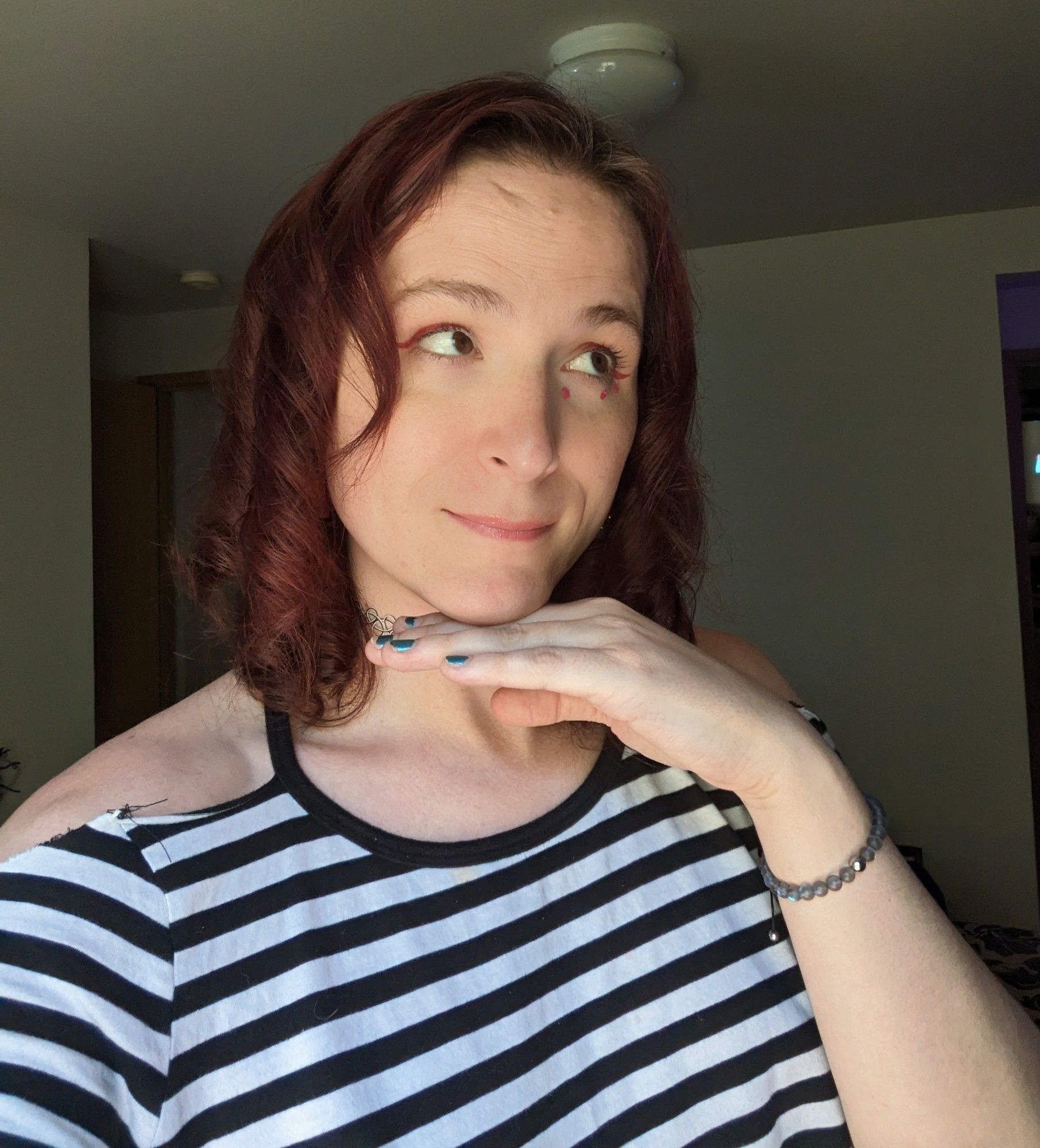 Selfie of Jacey with her hand popped beneath her chin, looking off to the side with her red hair curled and looking all cute