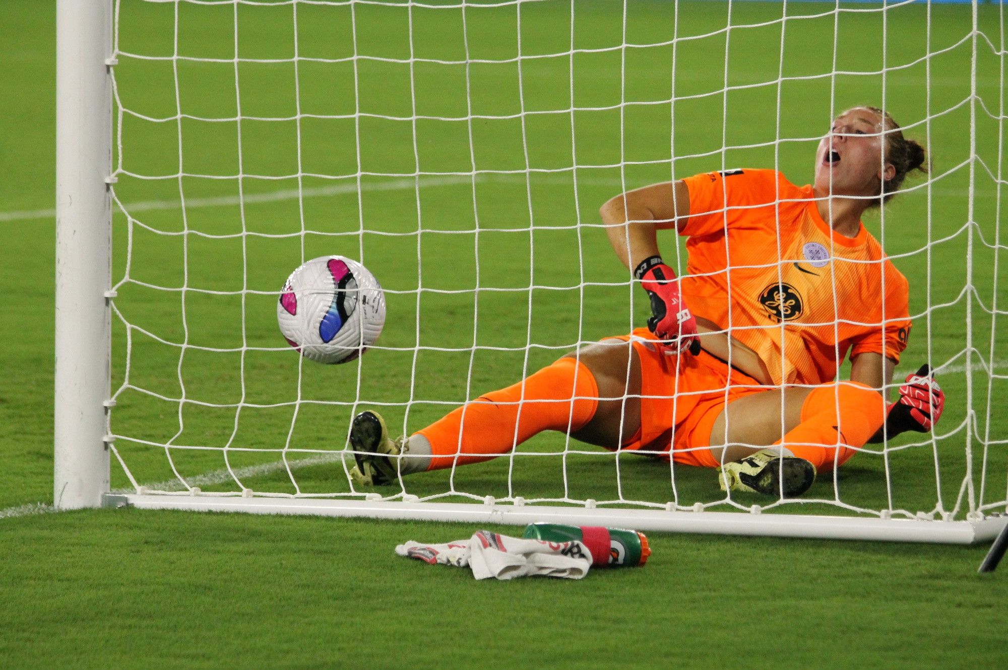 Racing Louisville goalie Jordyn Bloomer on the ground with her mouth hanging open in the moments after giving up a goal. The ball is to the left of her, just inside the net.