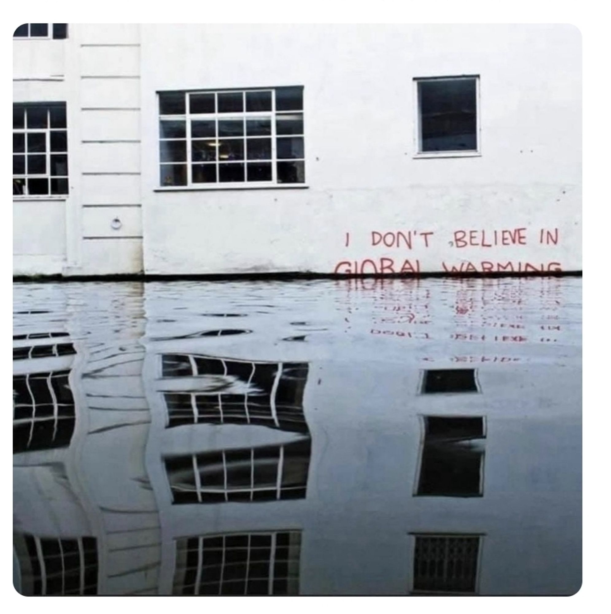 Haus, an dem Hochwasser steht. An der Wand ein Graffiti: I don't believe in global warming- ich glaube nicht an Erderwärmung