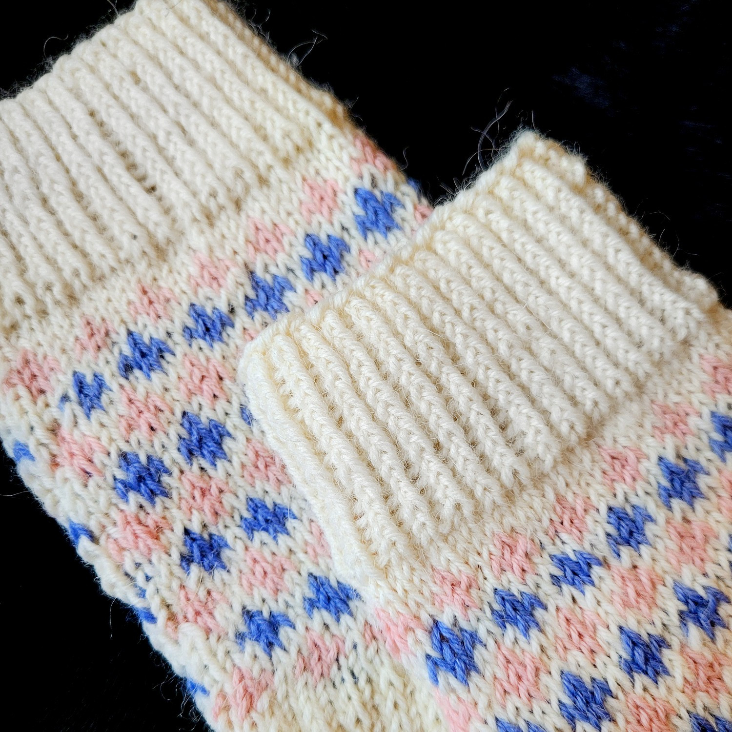 A detail of the socks. A pattern of pink and blue fleur de lis extends through the sock, with the exception of the cuff being white.