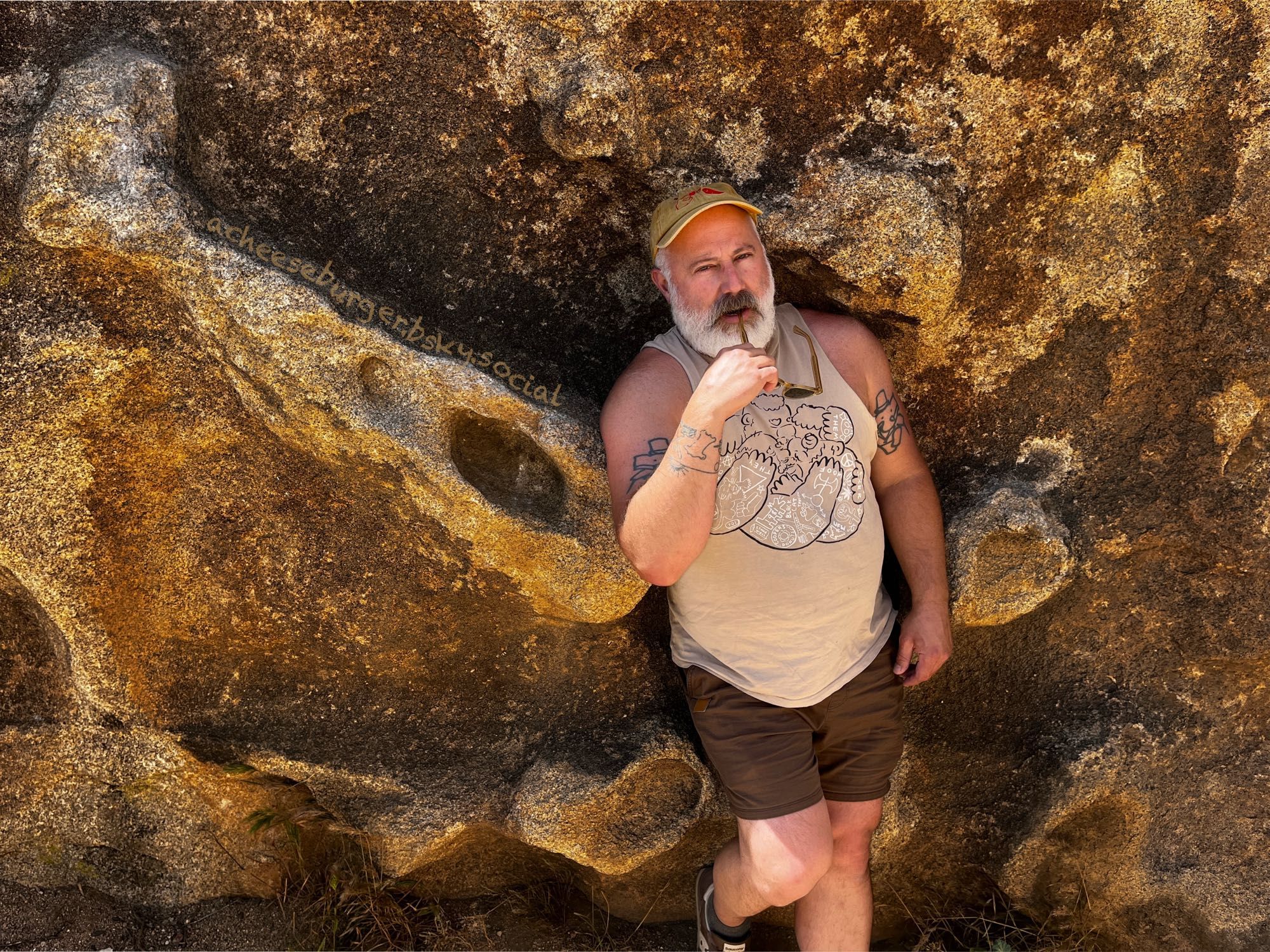 a grey bearded man leaning on a giant boulder