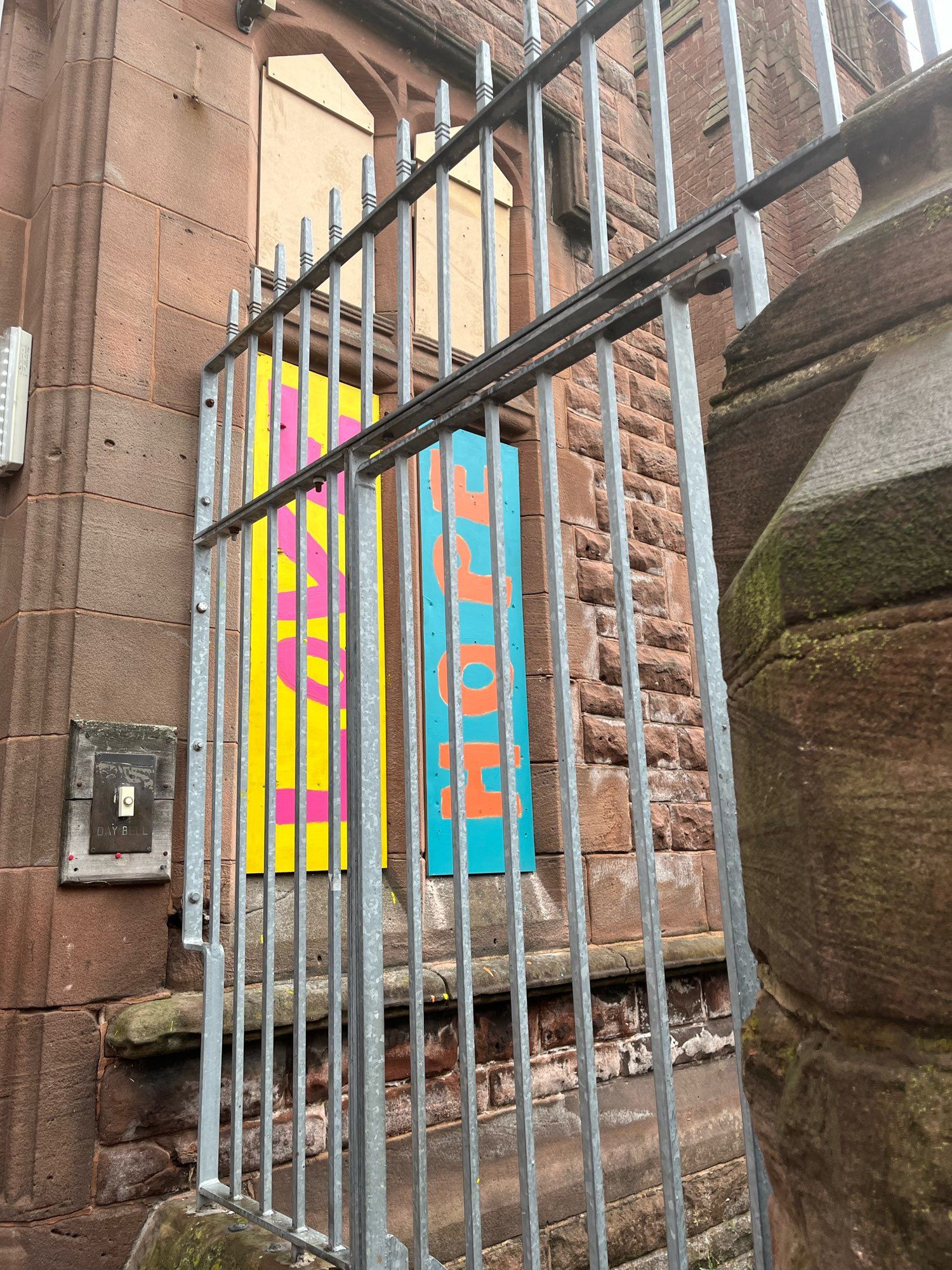 View through a gate of signs reading love and hope. Pink on yellow & orange on blue.